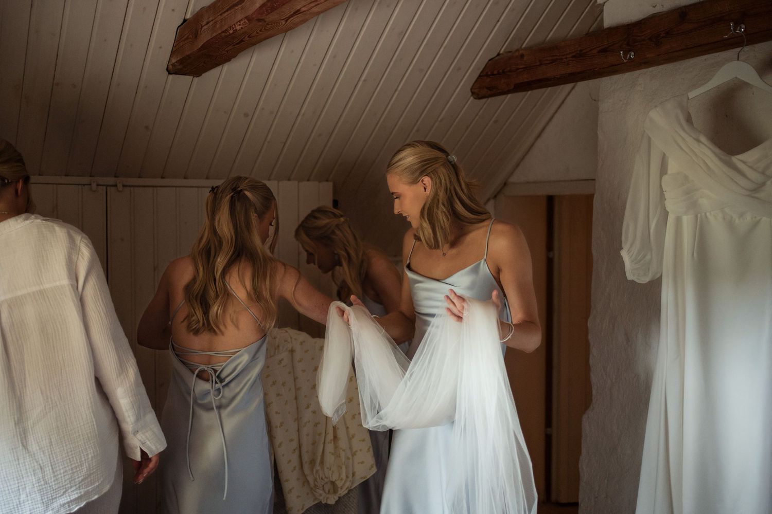 A series of white wedding dresses displayed in a rustic wooden room with exposed beams and natural lighting.