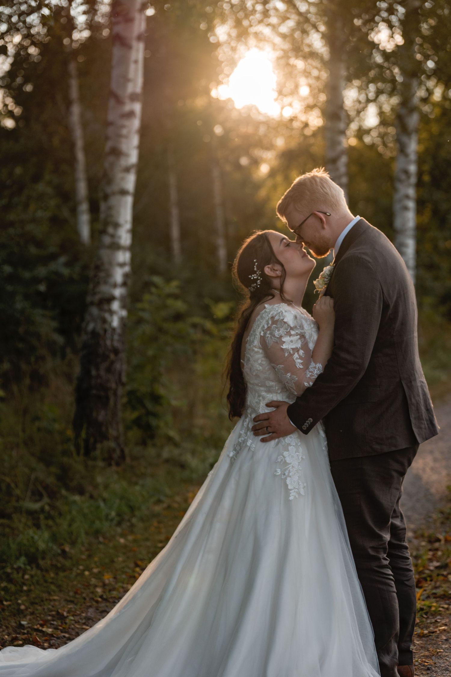 A romantic wedding couple embraces in a sunlit forest with birch trees during golden hour.