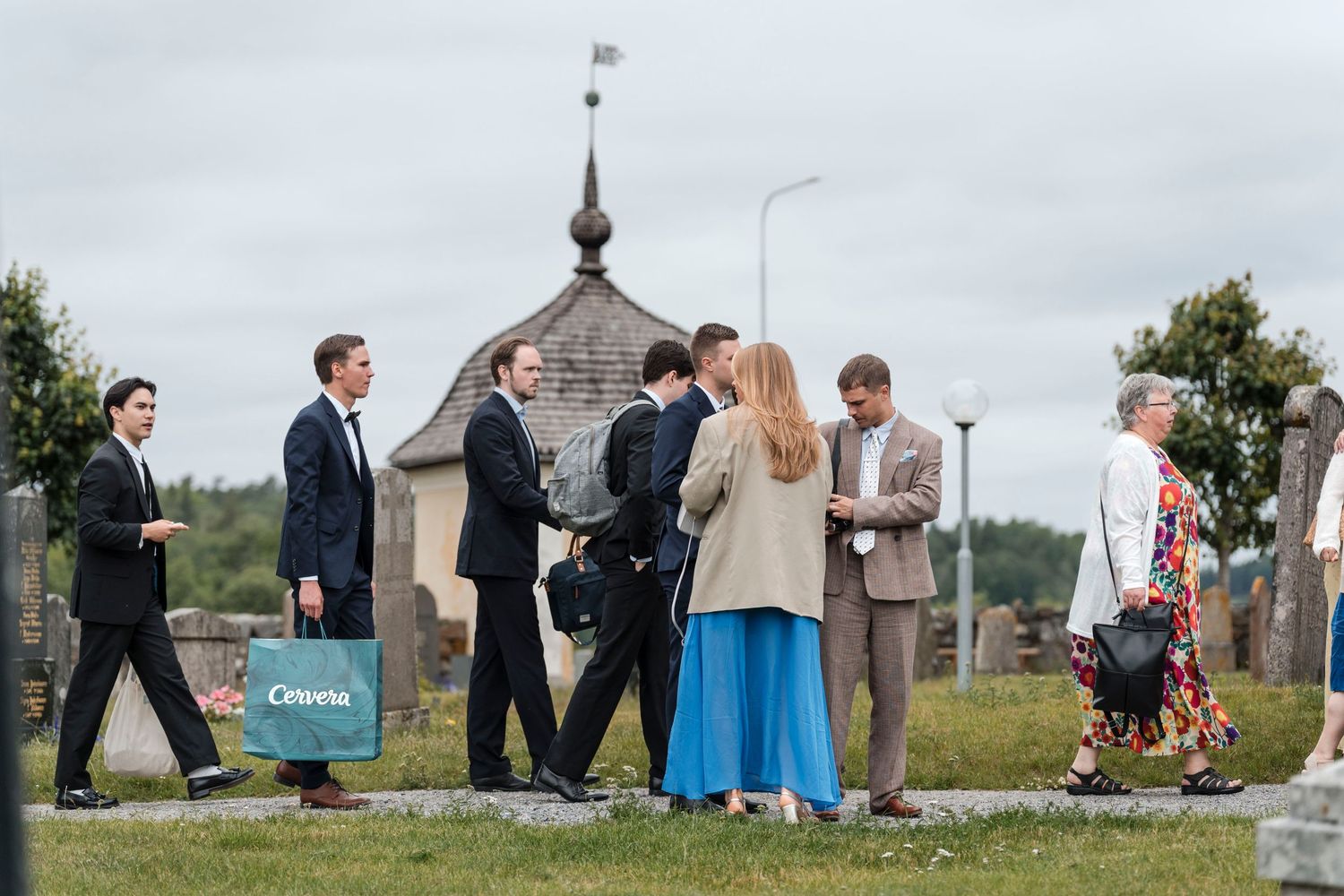A group of people gathered outdoors at a cemetery or church grounds, with a steeple visible in the background.