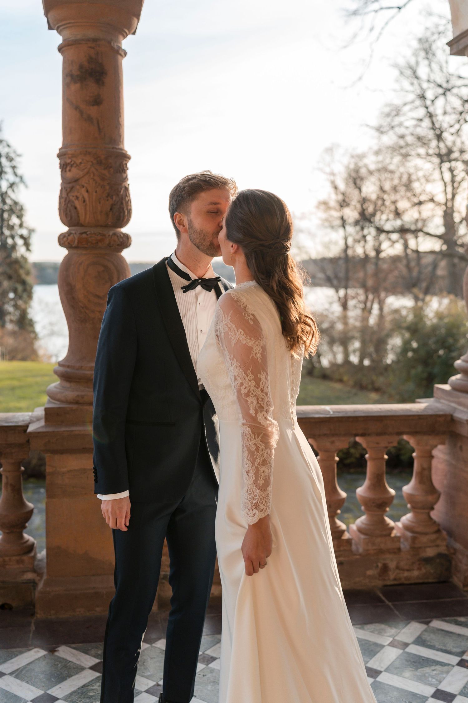 Elegant couple shares romantic moments on a terrace with ornate stone columns at sunset.