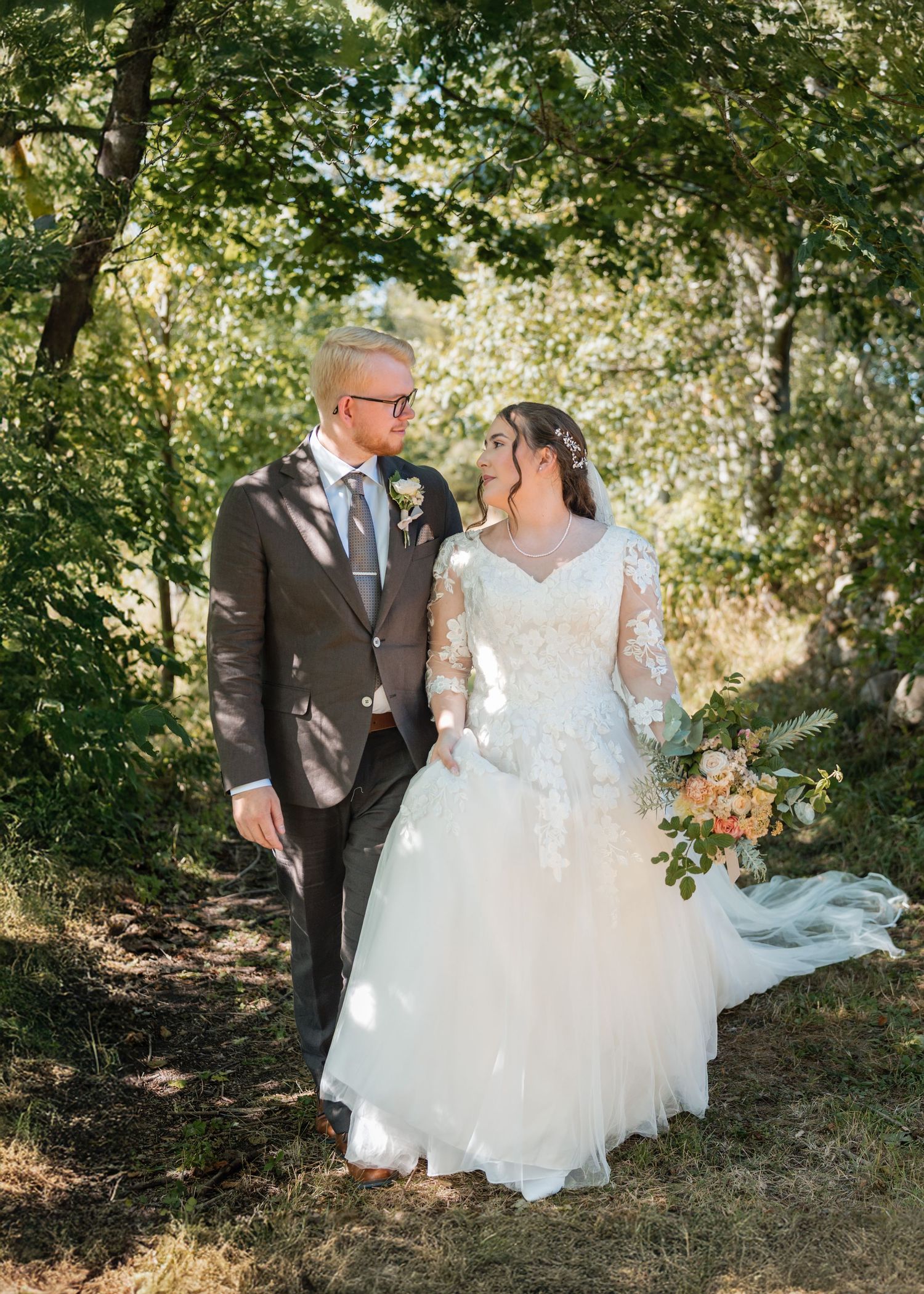 A couple shares an intimate moment under dappled sunlight in a lush forest setting during their wedding photoshoot.