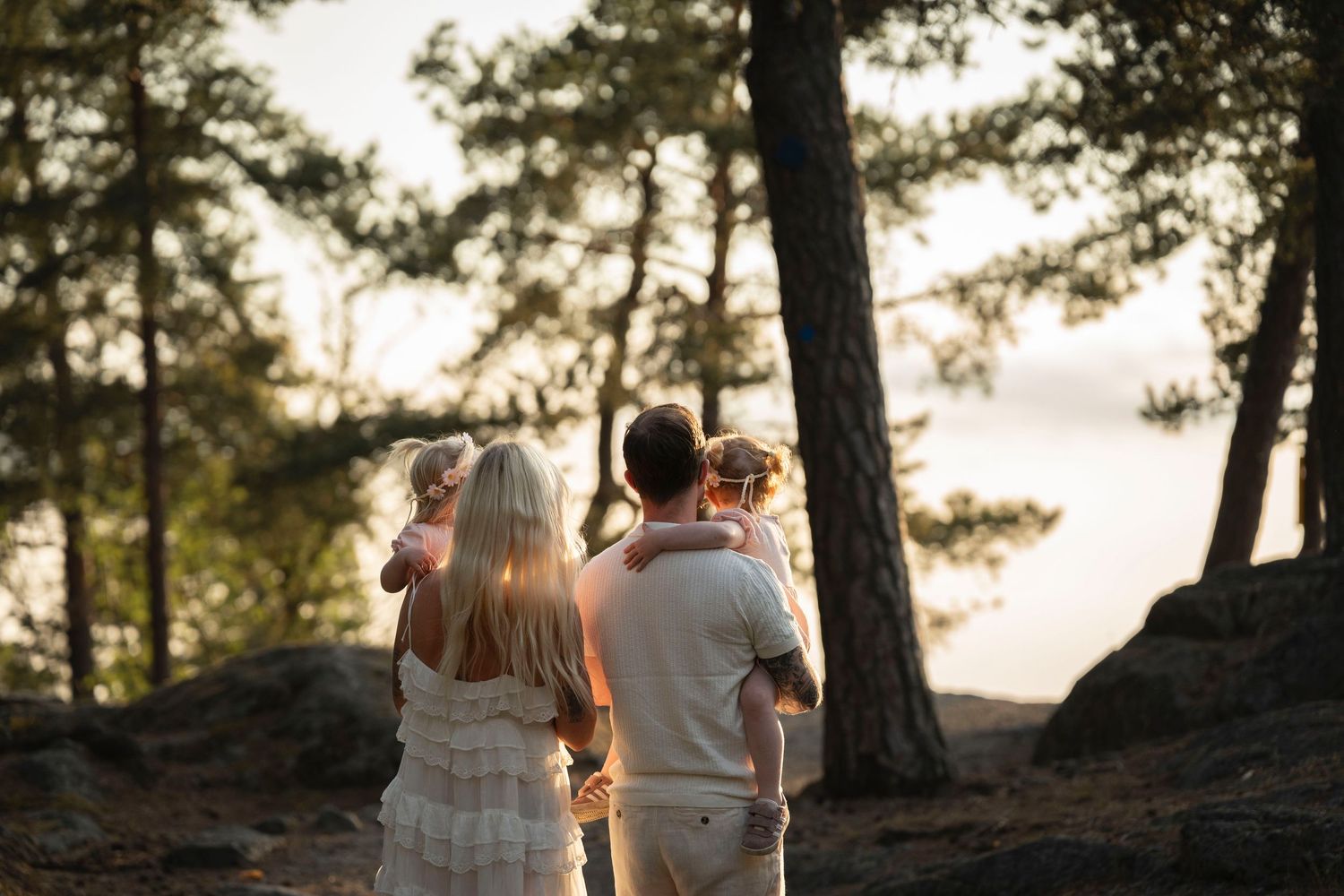 A couple sits together on a rocky cliff overlooking a scenic forest landscape at sunset.