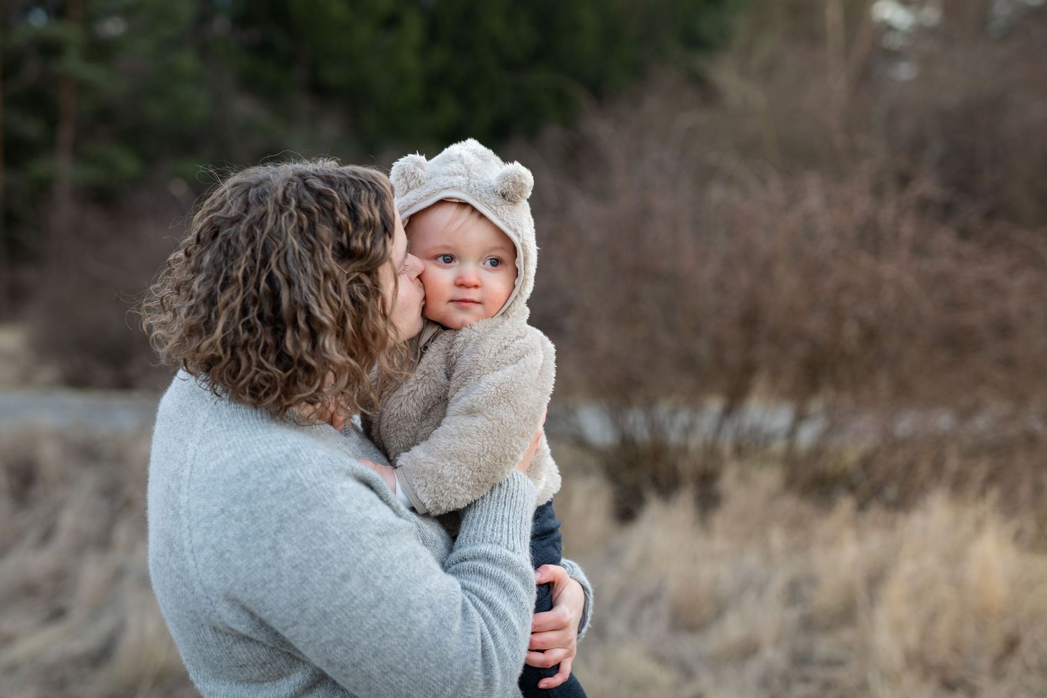 A tender moment between parent and baby wearing a knit hat outdoors on a winter day.