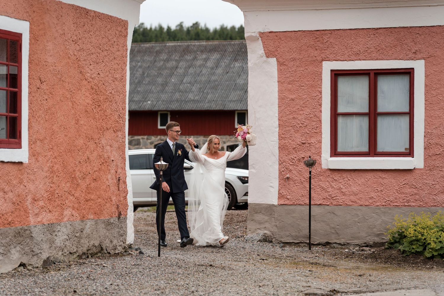 A bride and groom dance and twirl together outside a pink stucco building with white trim.