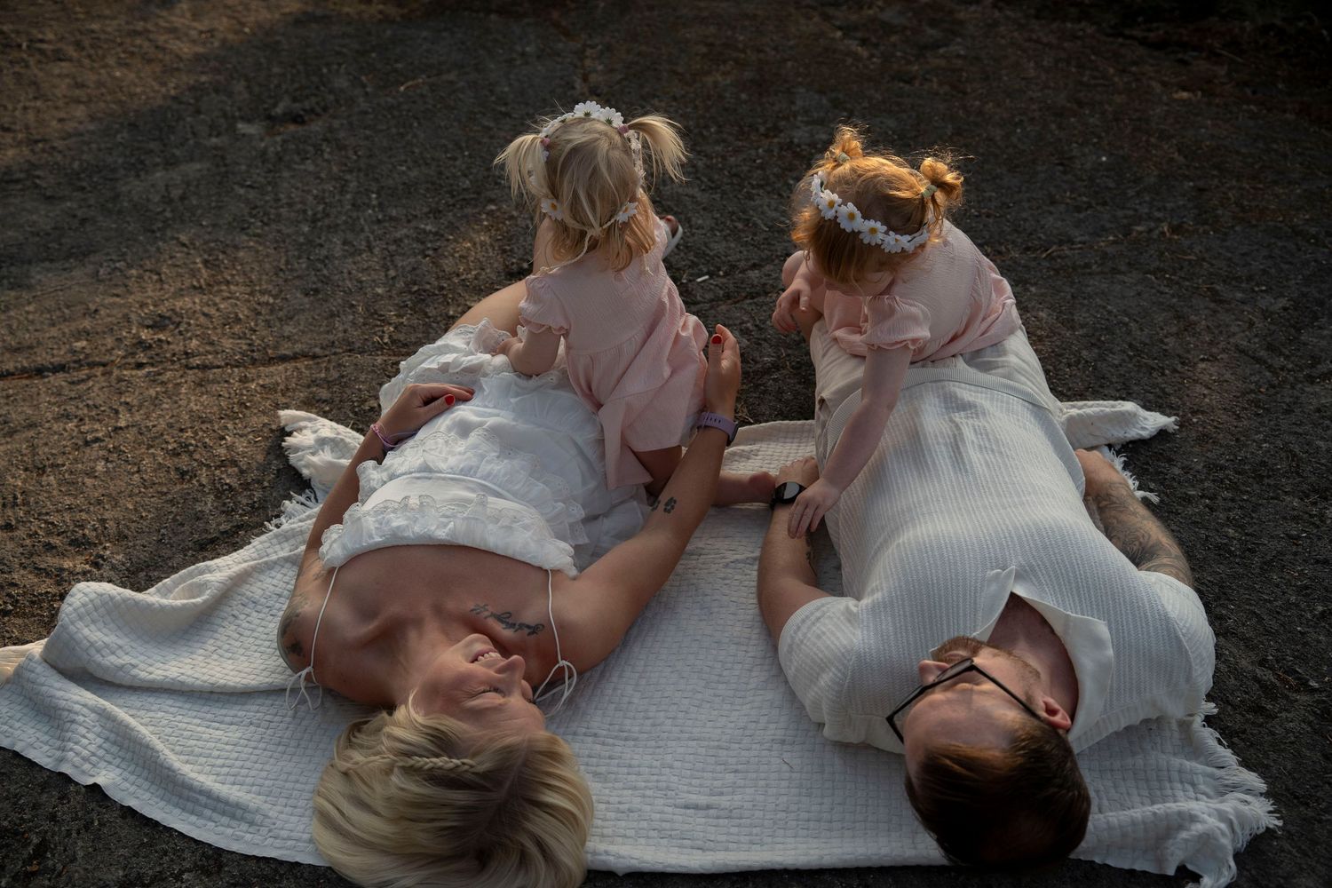 Two people in wedding attire lay on a blanket in a grassy field during sunset.