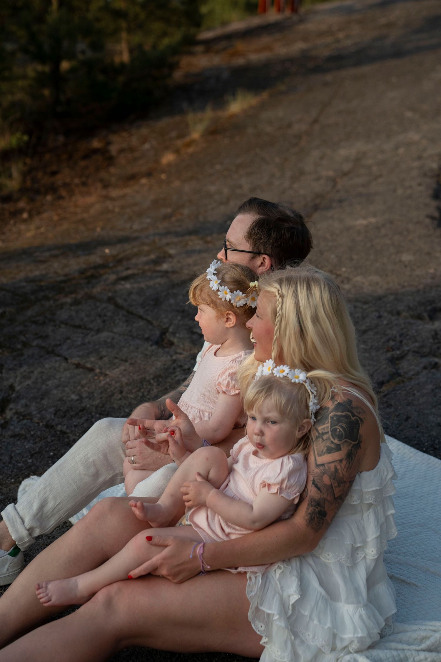 Family relaxing together on white blanket outdoors at sunset during photo session.