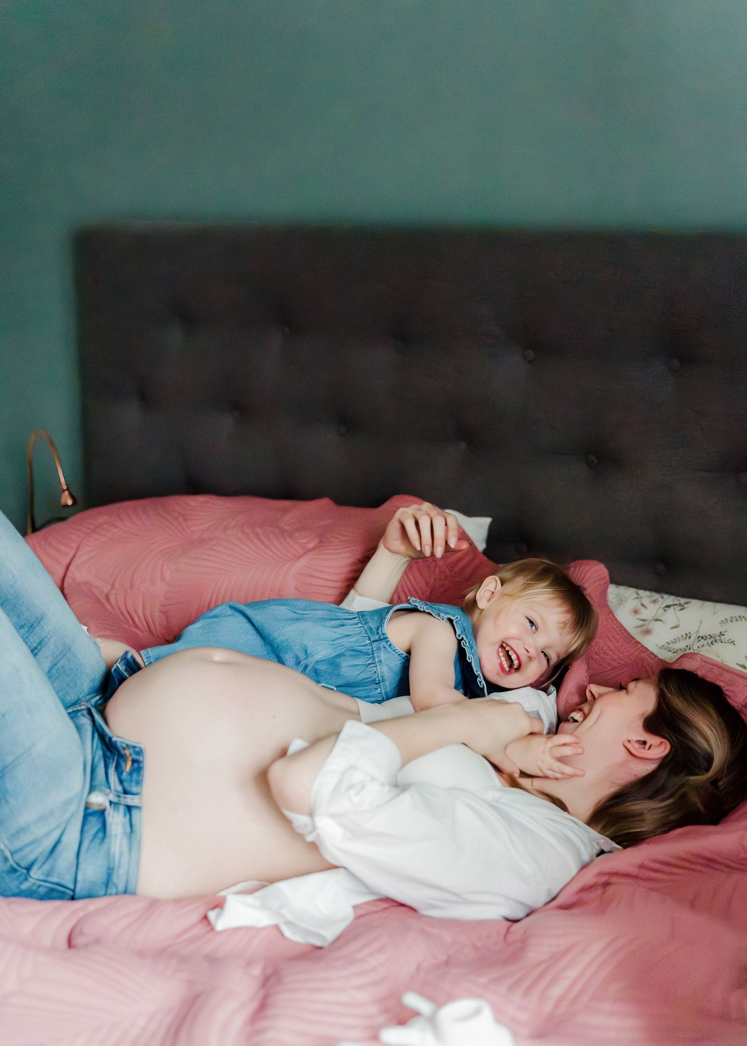 Pregnant woman resting peacefully on pink bedding while wearing light blue clothing.
