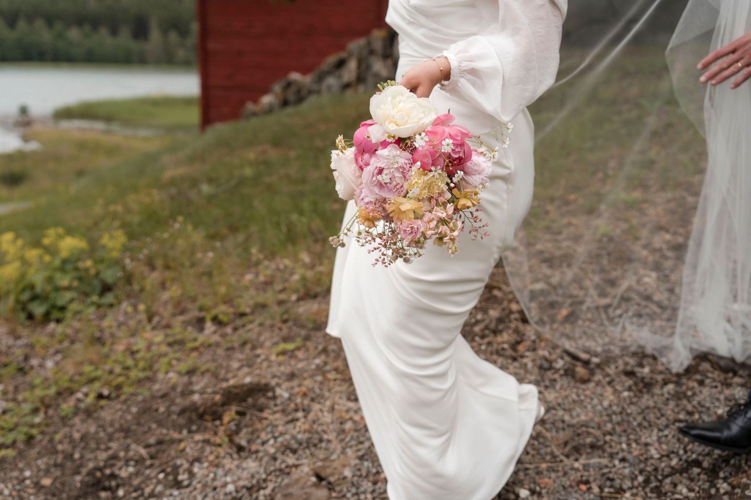 A person in a white wedding dress walks through a rustic outdoor setting with scattered flower petals on the ground.