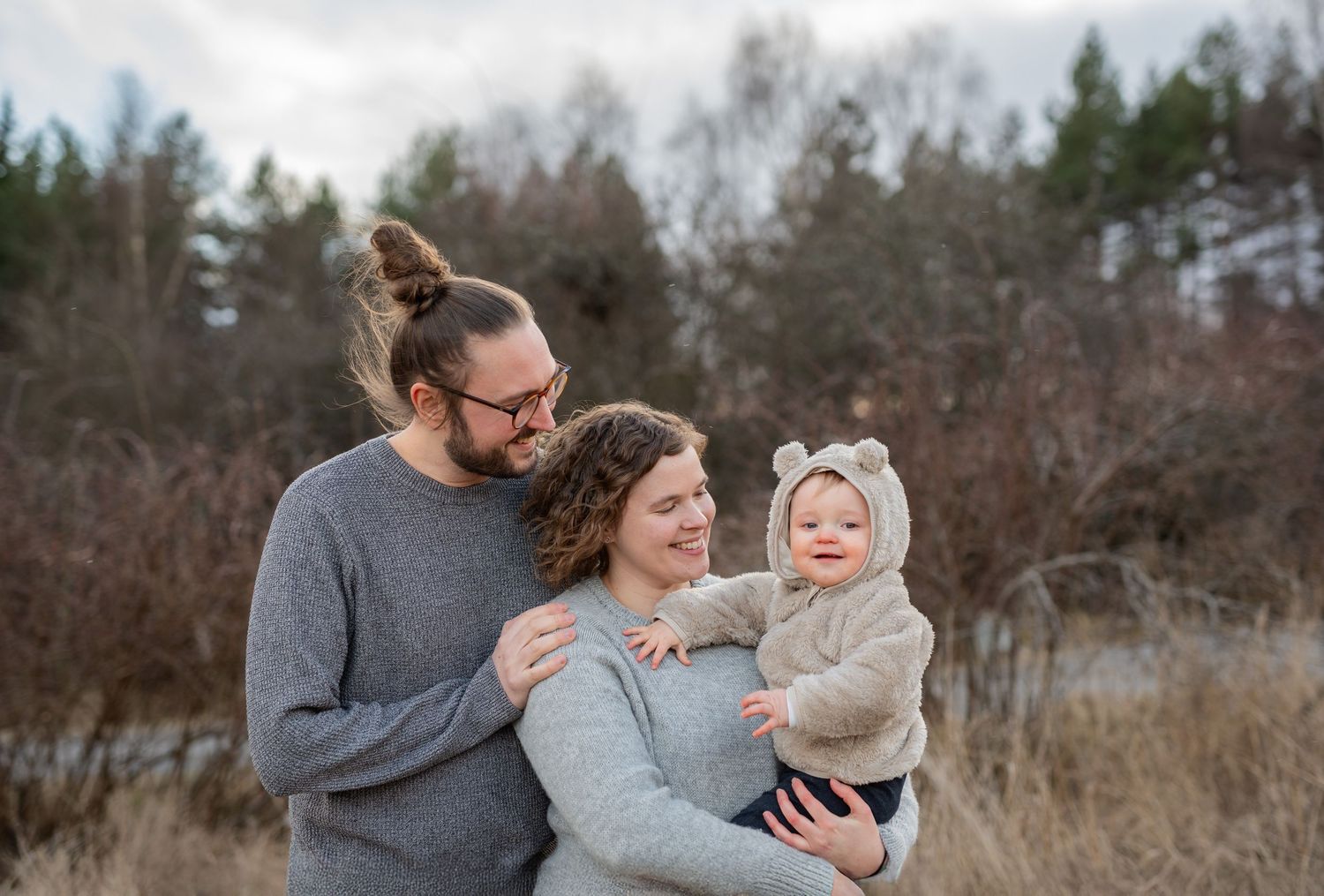 A family shares a tender moment together outdoors in a natural setting with tall grass and trees in the background.