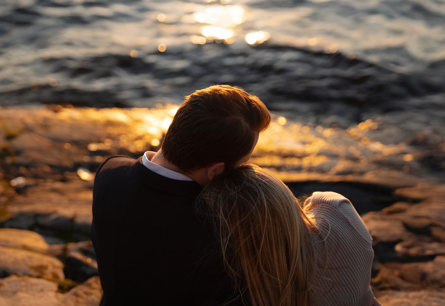 A couple sits together watching a golden sunset over rippling water.
