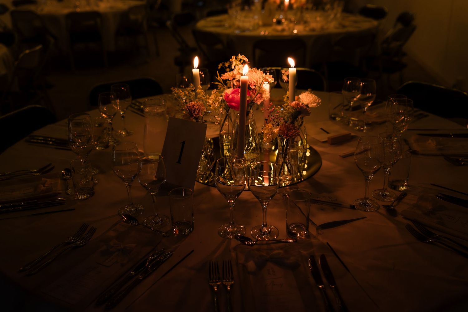Elegant dining table settings with glowing candles and floral centerpieces create a romantic ambiance for an evening event.