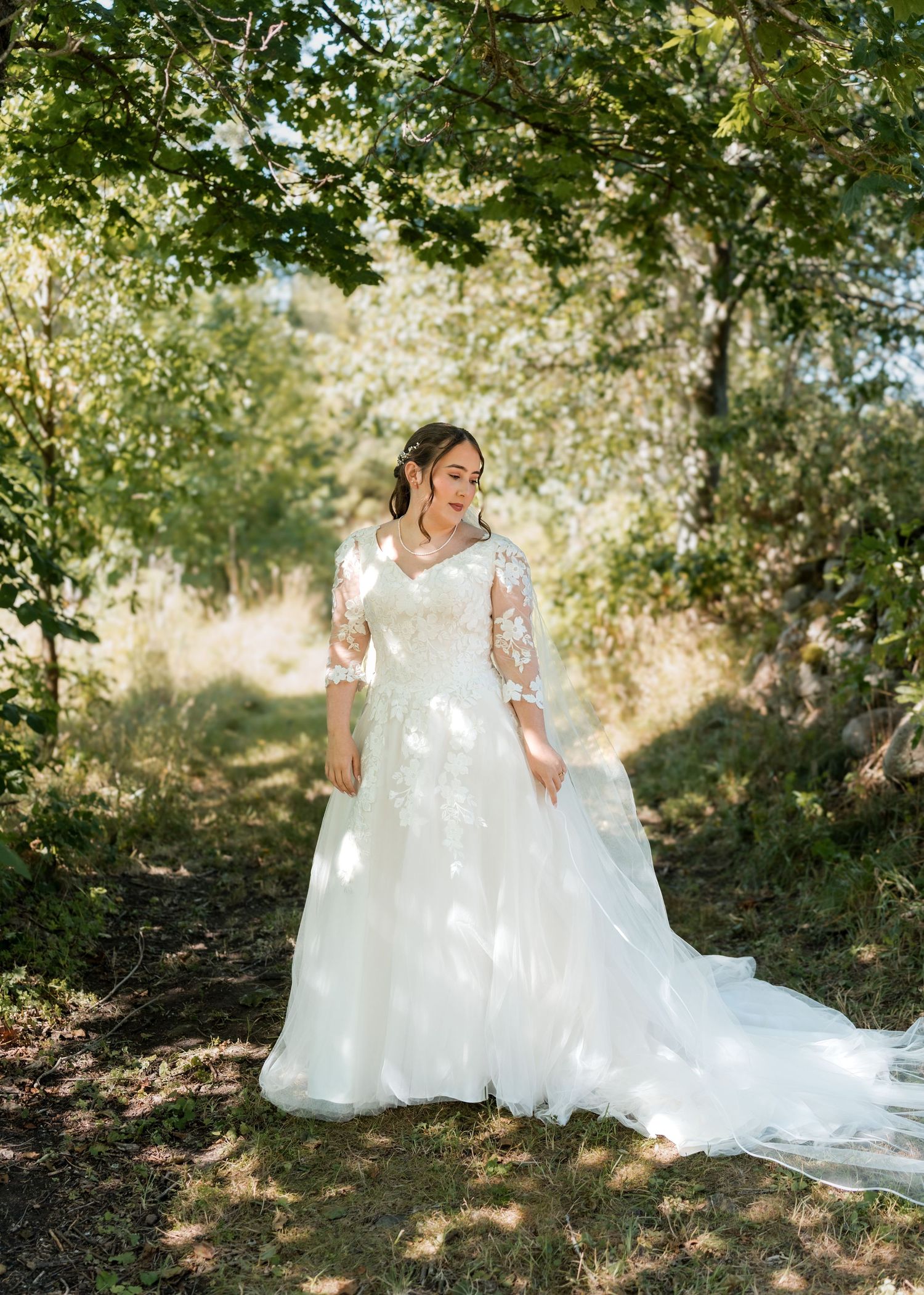 Elegant white wedding dress photographed in dappled sunlight under trees in a garden setting.