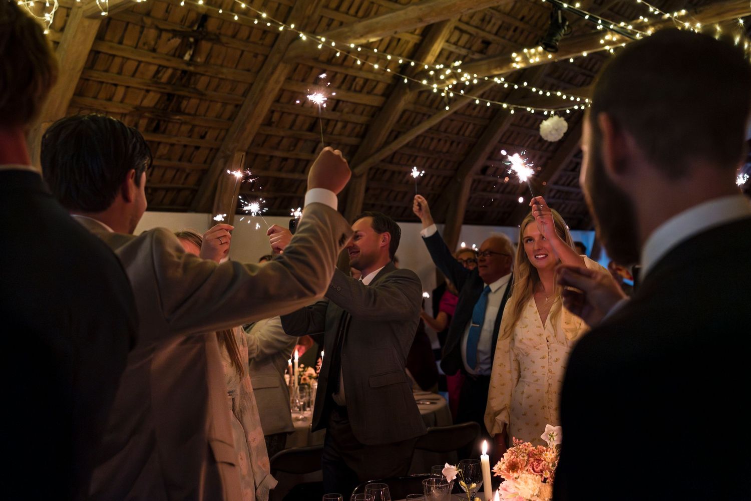 Wedding guests dancing and celebrating at a dimly lit reception venue decorated with twinkling lights.
