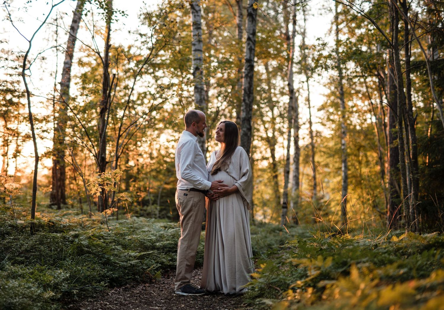 A couple embraces in a sun-dappled autumn forest with golden light filtering through the trees.