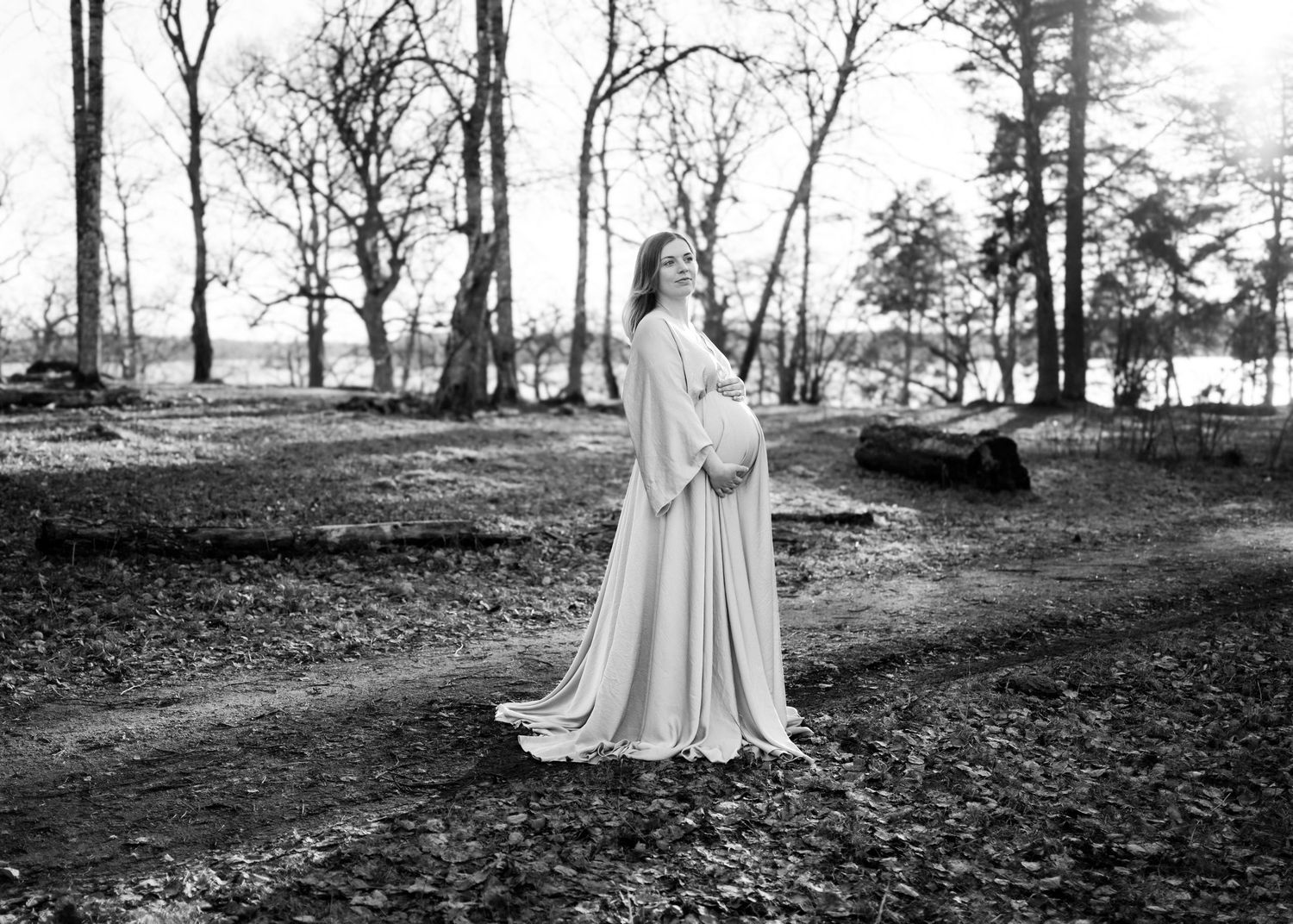 Woman in flowing white gown standing in a black and white forest landscape during winter.