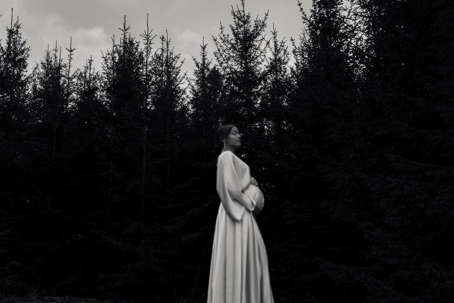A figure in a flowing white dress stands in a dark forest setting creating an ethereal and mysterious atmosphere.