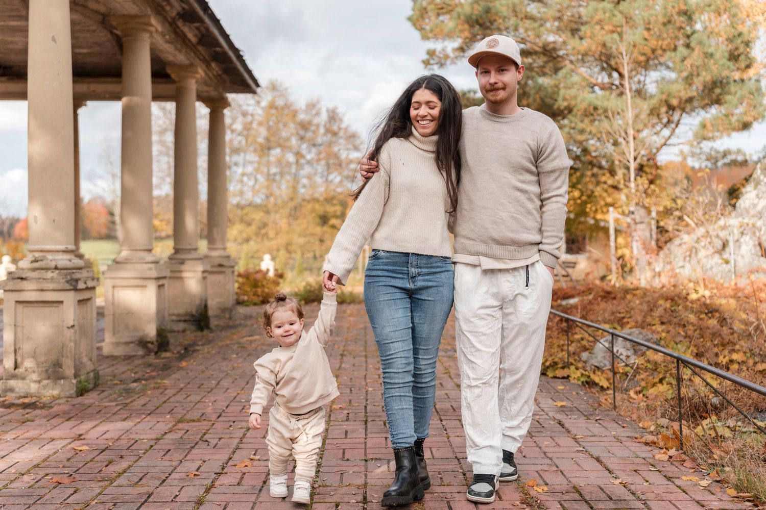 A family in matching beige and white outfits walks together on a brick pathway during autumn.