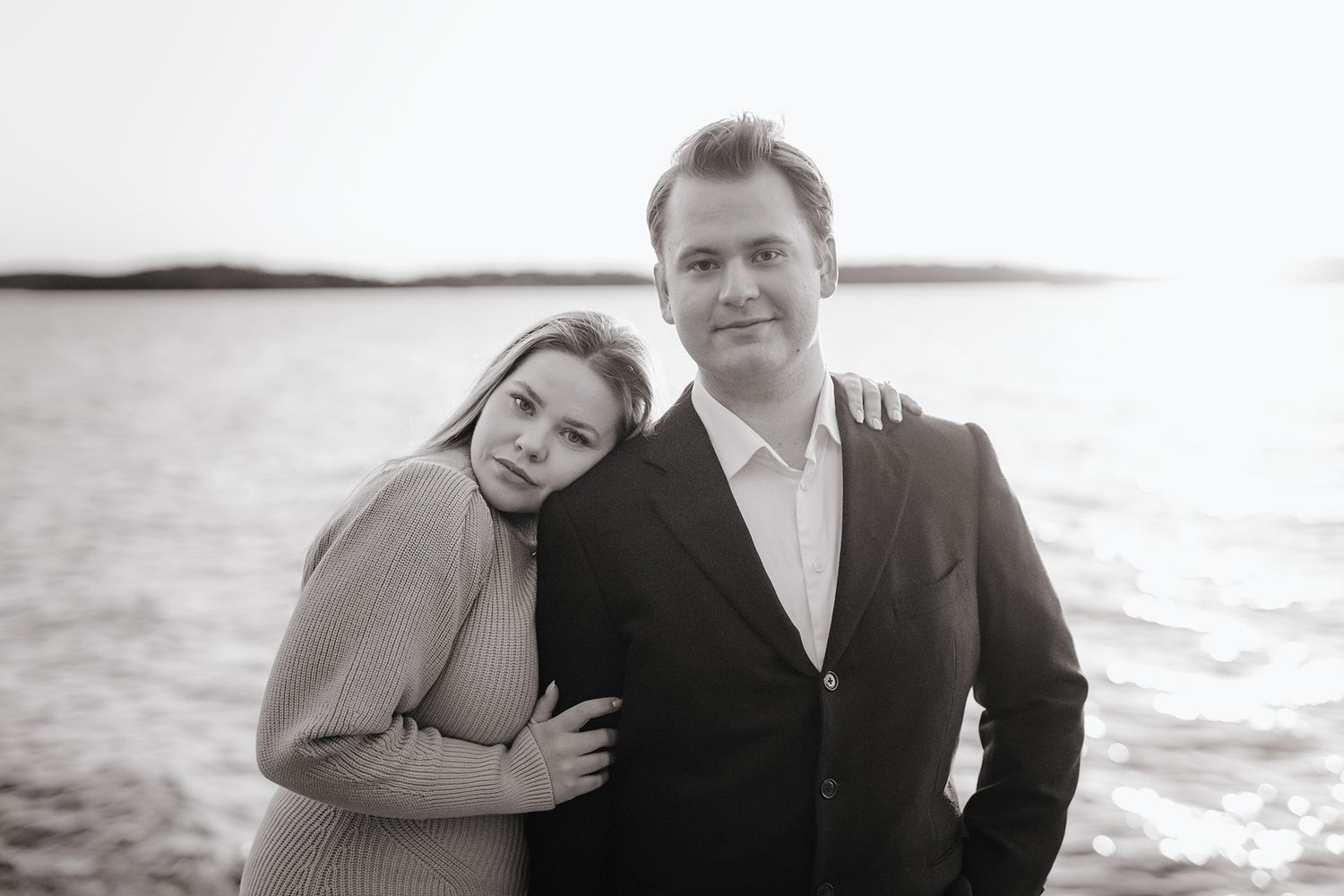 Ett par poserar för ett svartvitt porträtt vid havet i solnedgången.