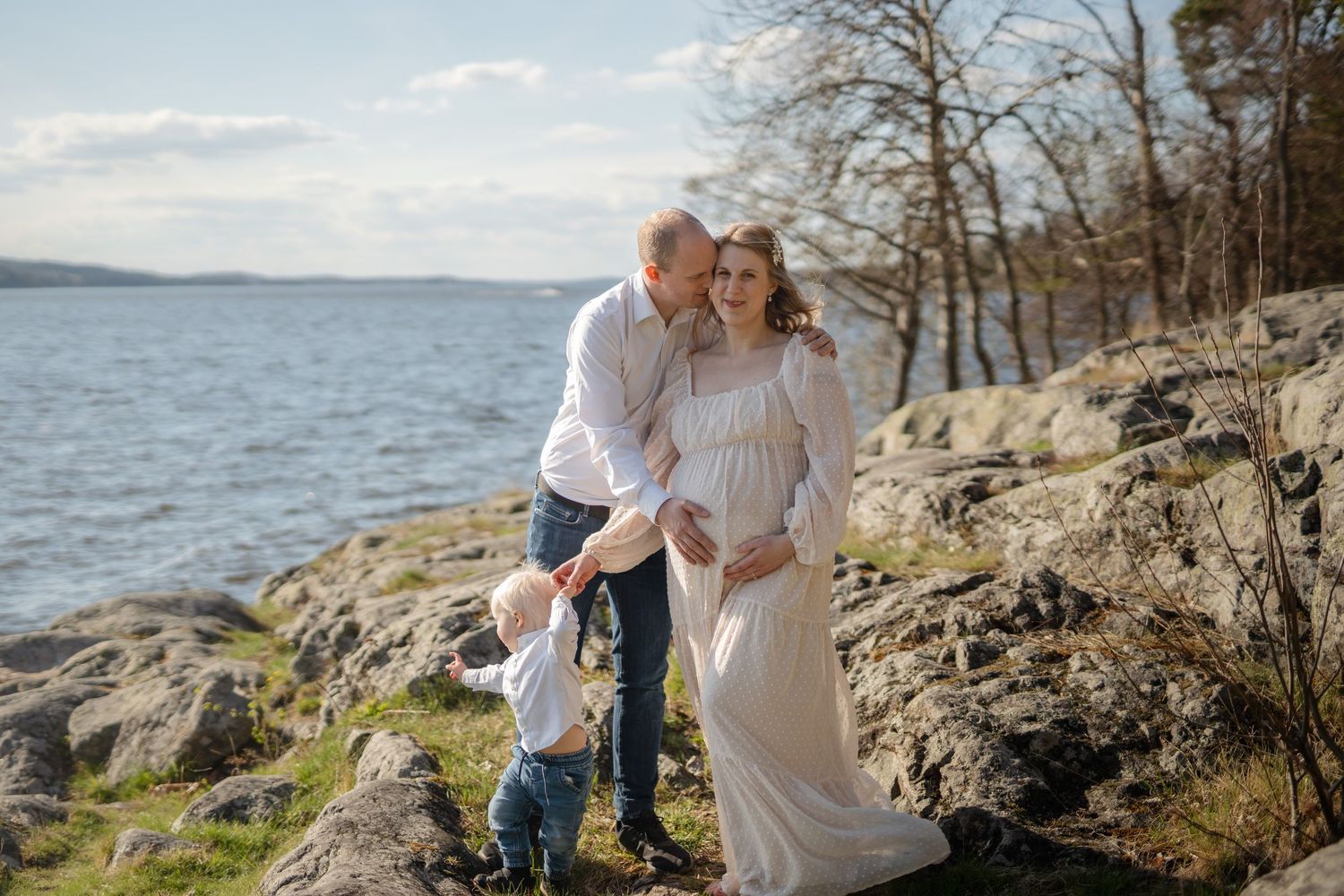 En familj delar ett ömt ögonblick tillsammans vid en stenig kustlinje.