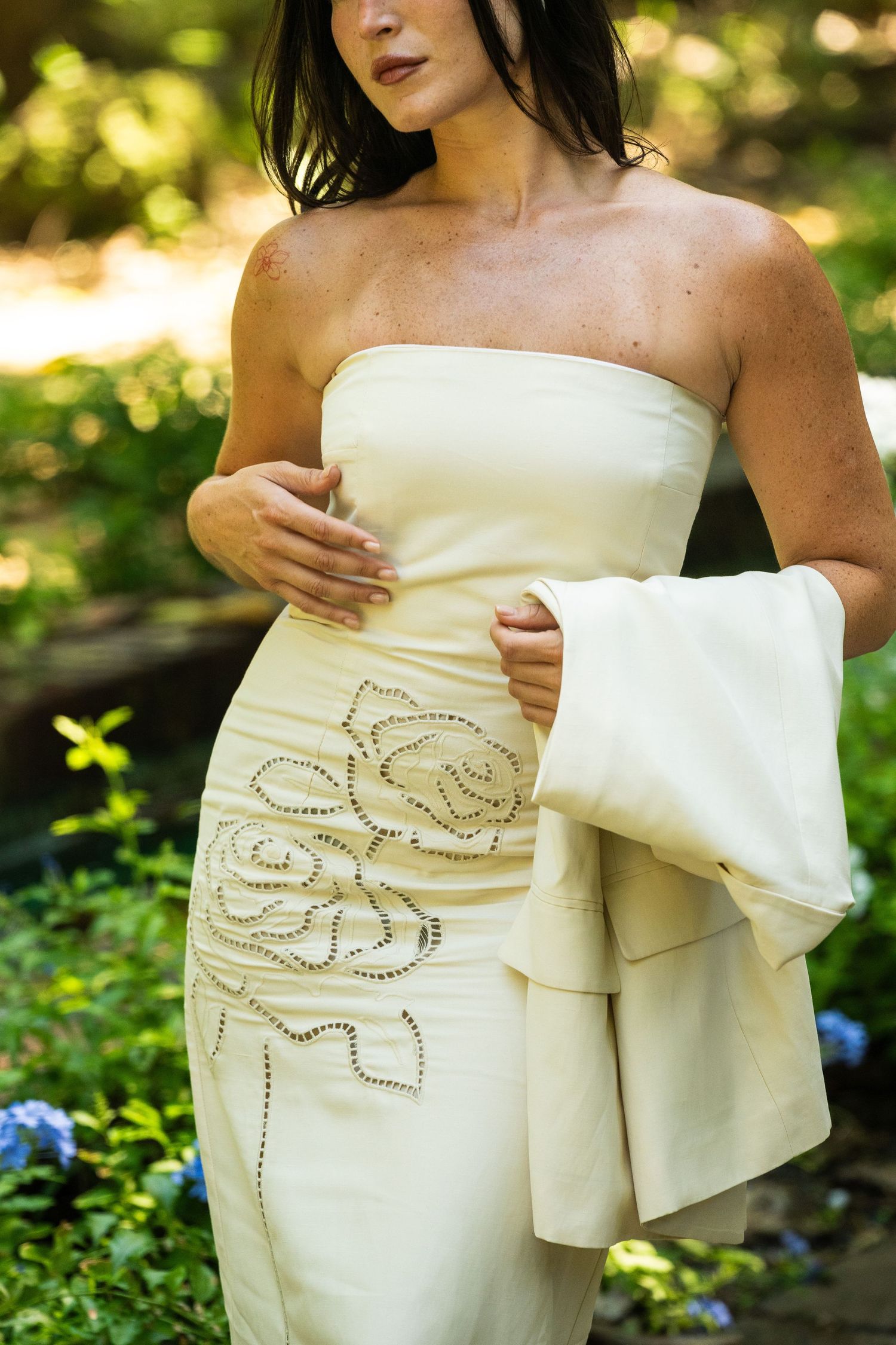 Woman in strapless cream gown with floral embroidery holds matching blazer.