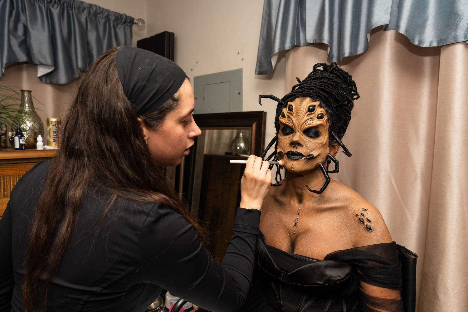 Makeup artist applying intricate gold and black face paint to a model with dramatic Halloween costume.