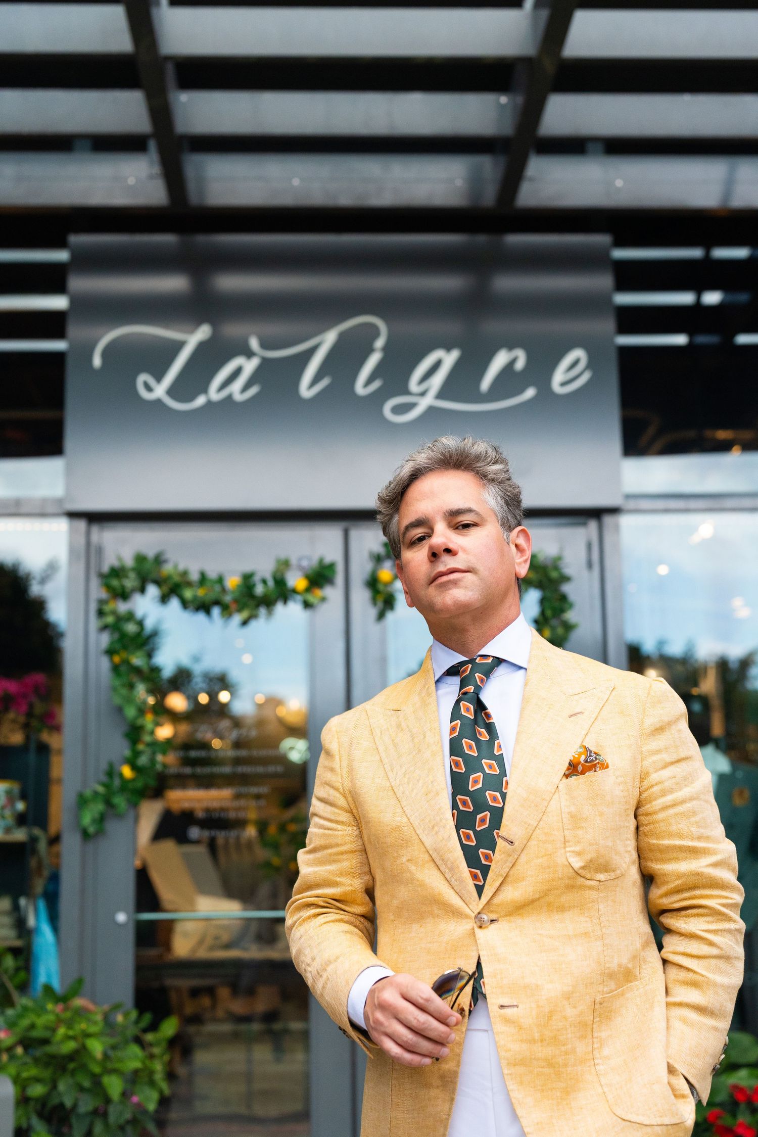Elegant man in yellow blazer and patterned tie standing outside La Tigre restaurant.
