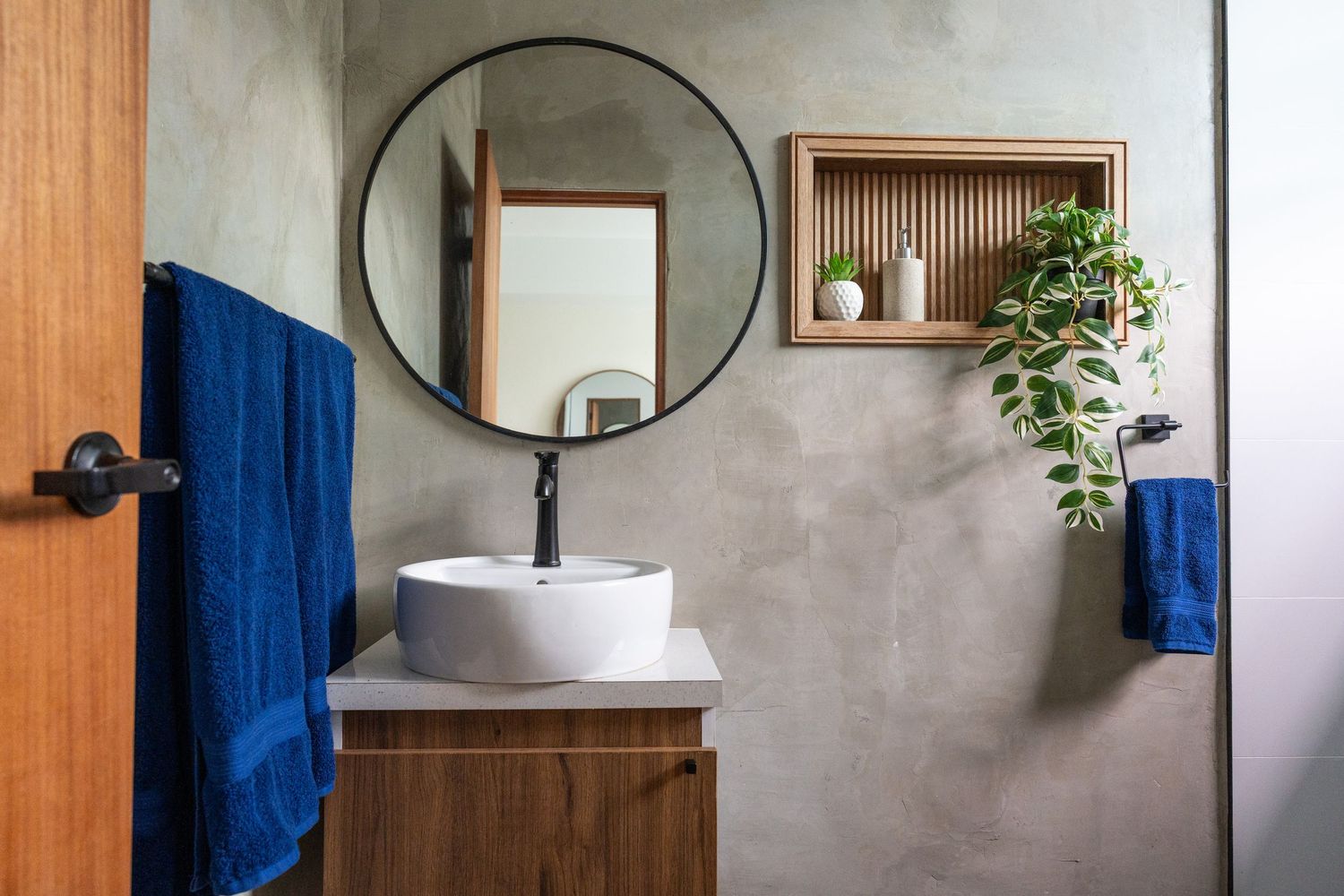 Modern bathroom vanity with round mirror, vessel sink, and blue towels on concrete walls.