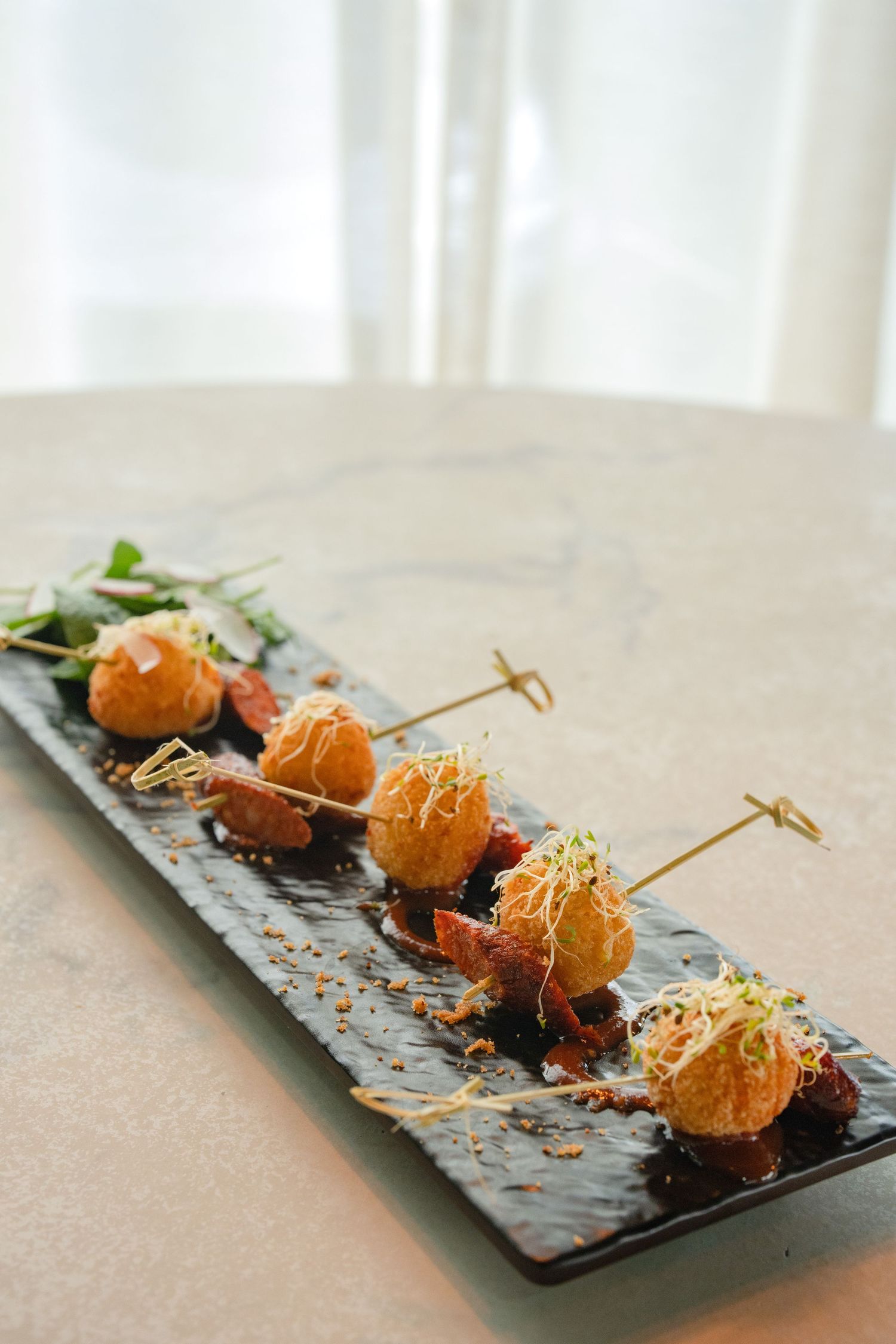 Gourmet fried appetizer bites on black slate plate garnished with microgreens and skewers.