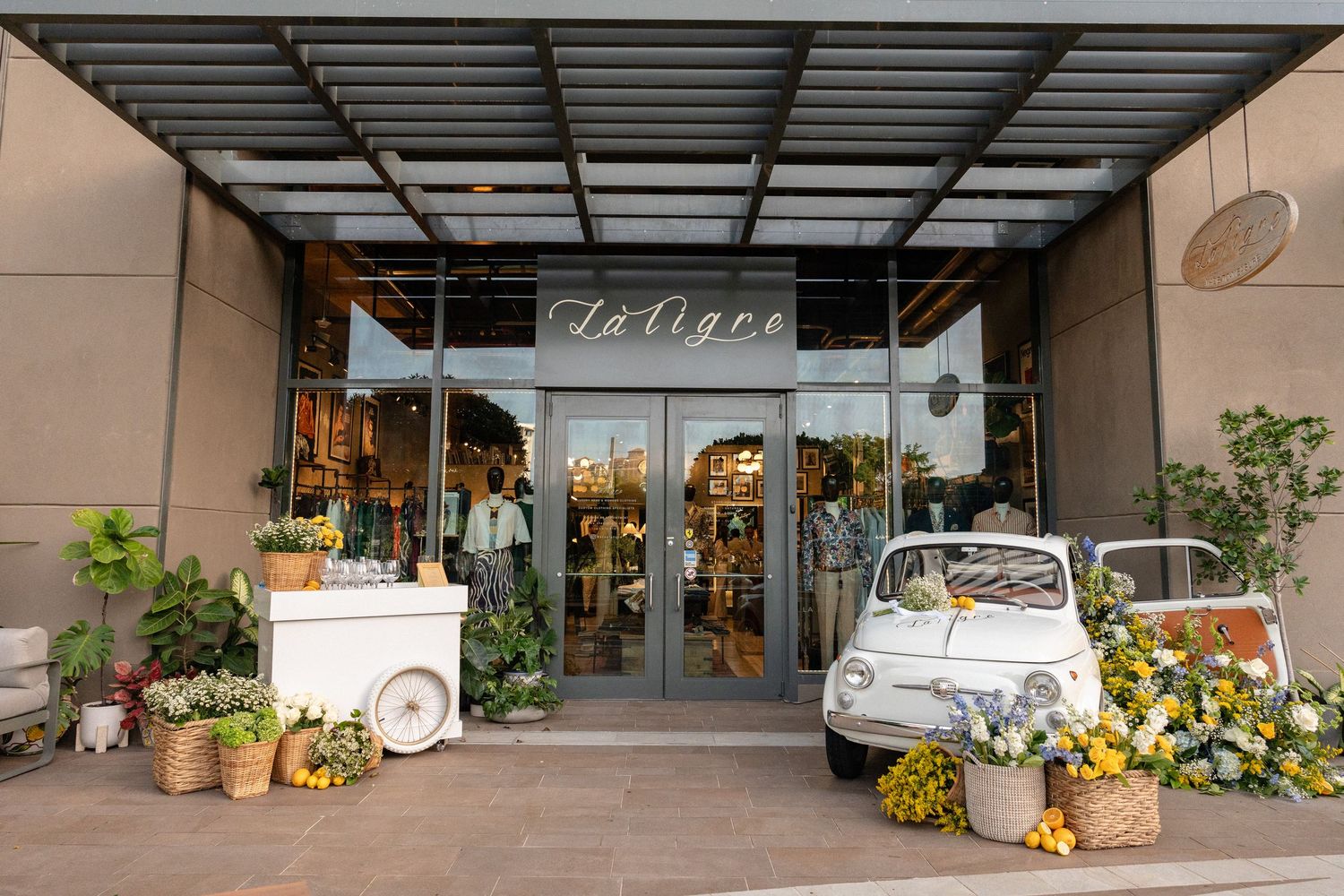 La Tigre boutique storefront entrance decorated with flowers and a vintage white Fiat 500 car display.