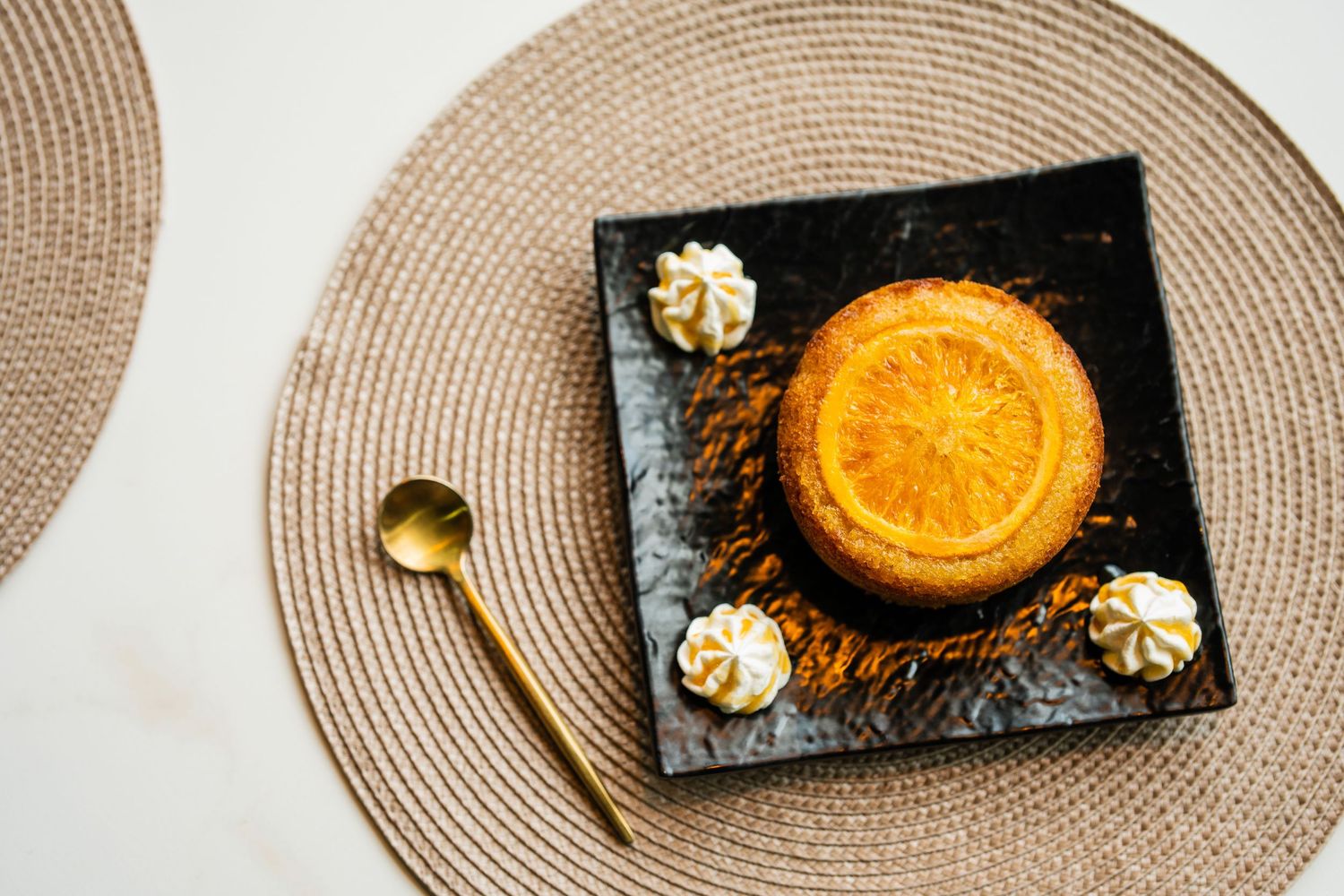 Elegant orange tart dessert topped with caramelized orange slice and cream rosettes on black plate.