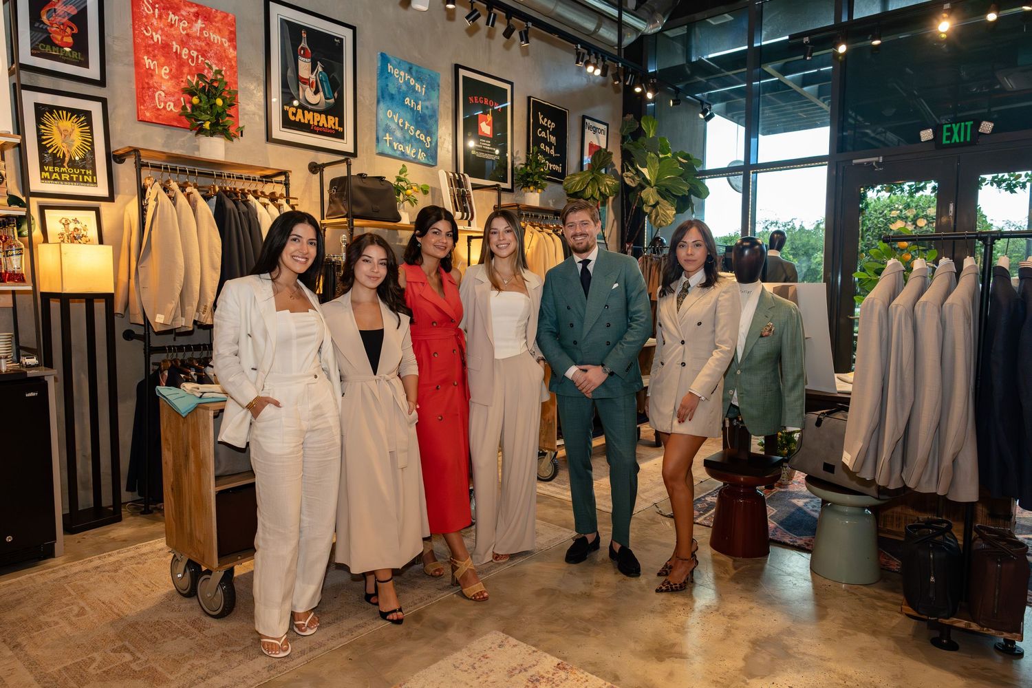 Group of seven people posing together inside a stylish menswear clothing retail store.