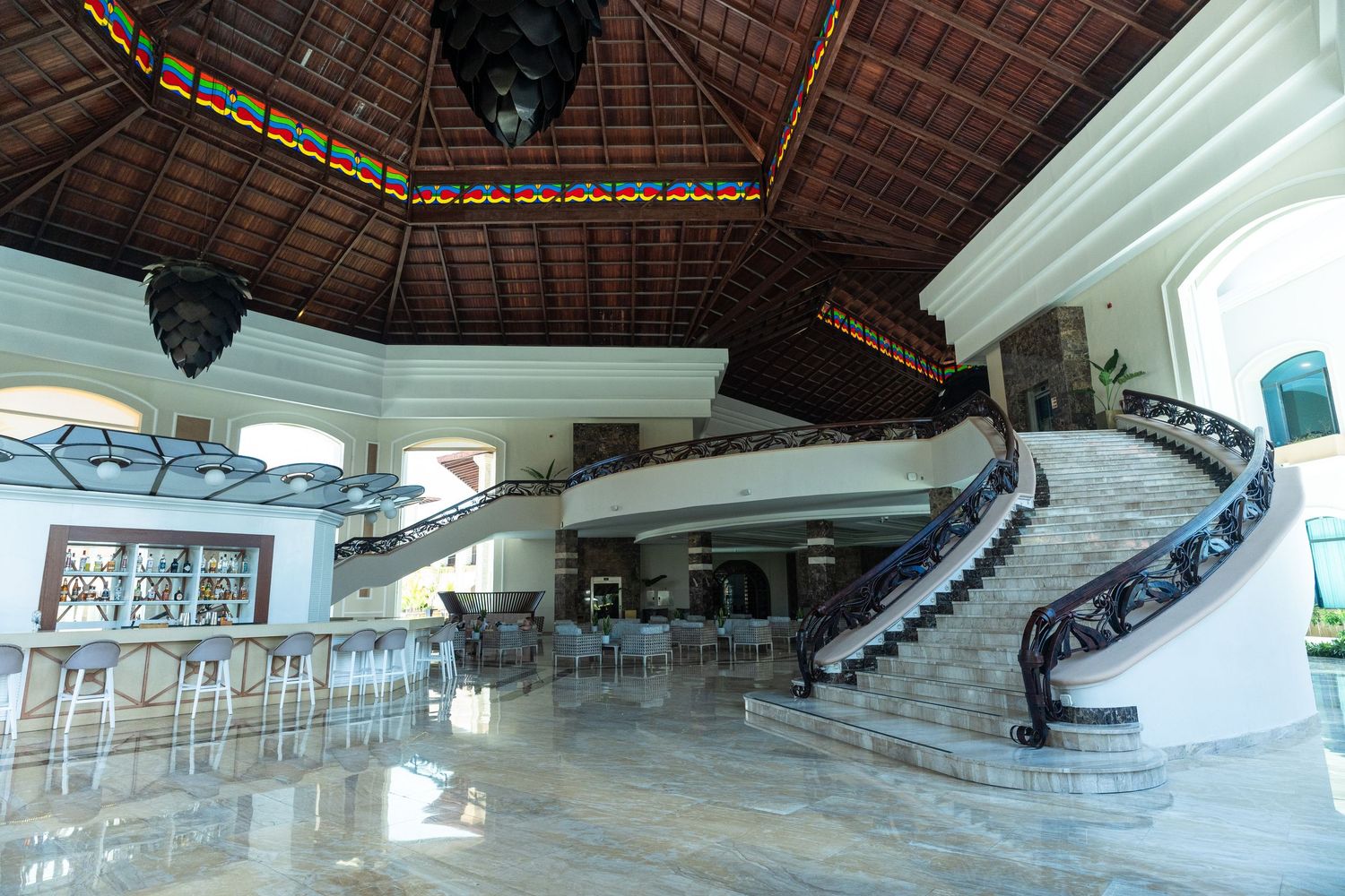Grand hotel lobby with elegant spiral staircase, marble floors, and ornate wood ceiling.