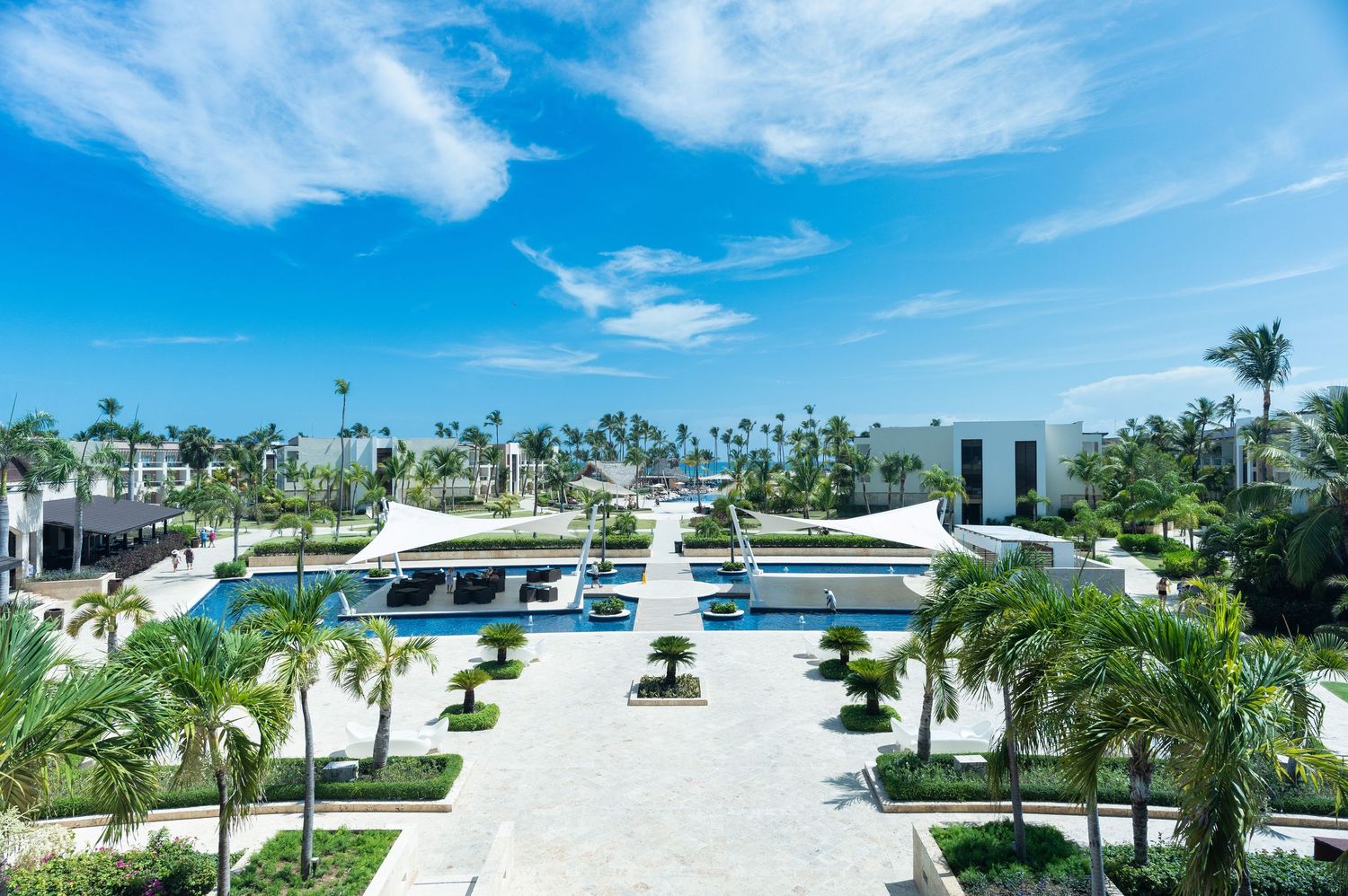 Aerial view of luxury tropical resort with palm trees, pools, and blue sky.