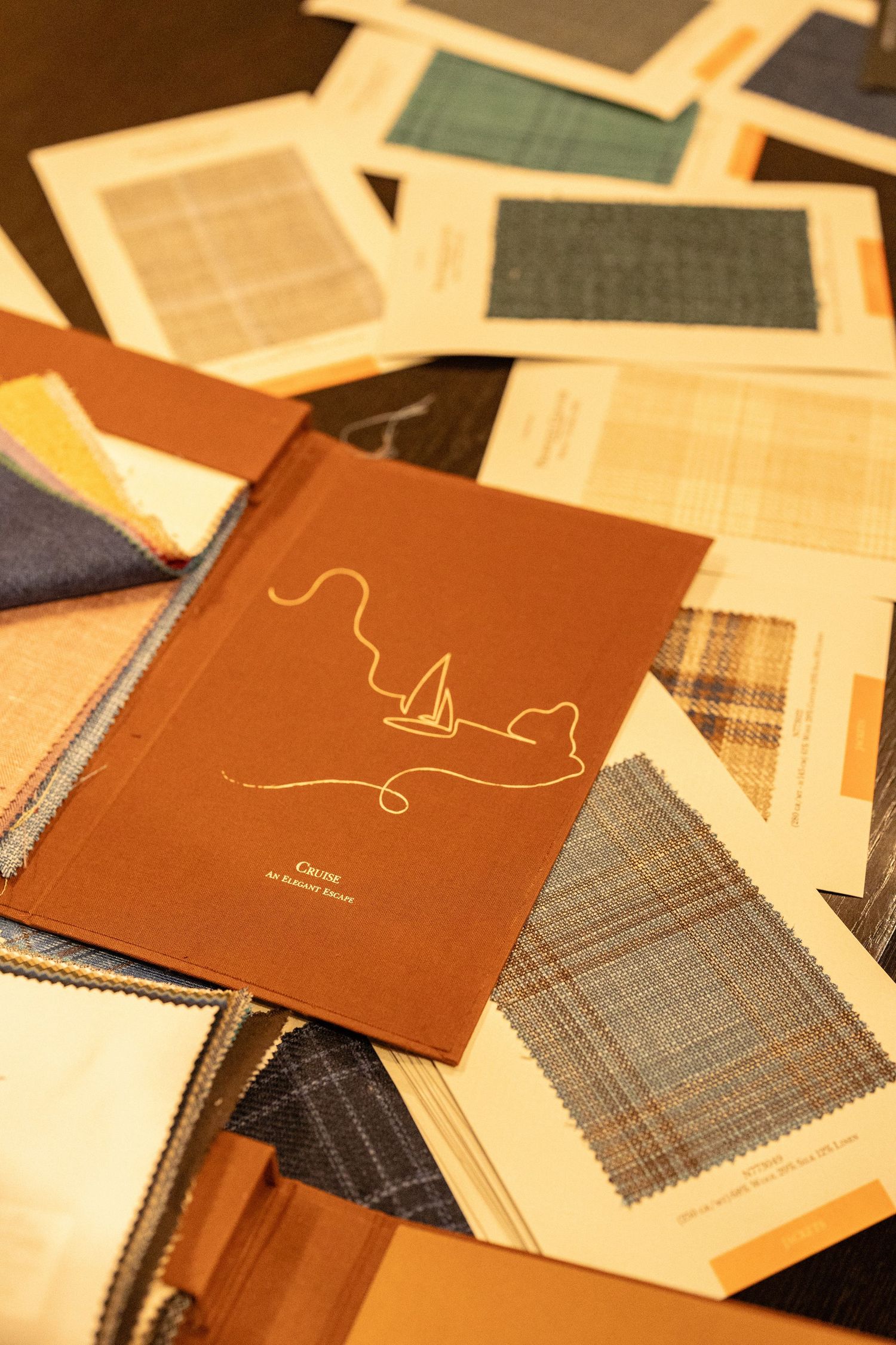 Fabric swatches and tailoring samples spread across a table with a brown Canoe by Alberto Nardi catalog.
