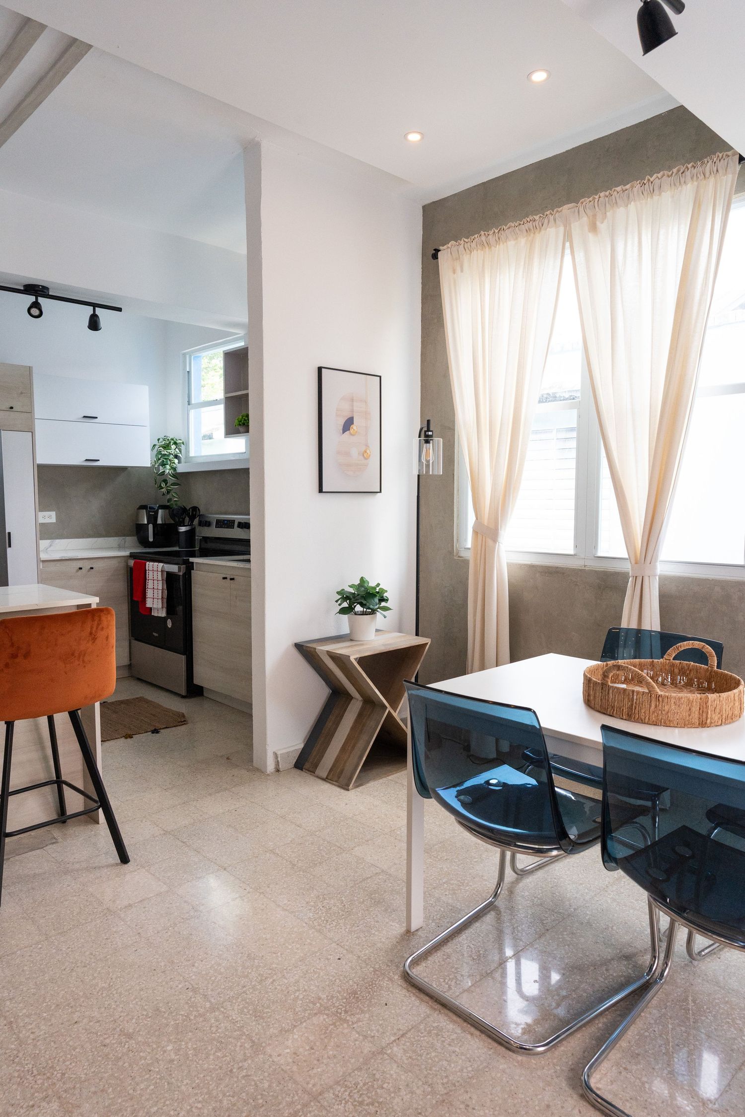 Contemporary dining area with blue chairs and kitchen visible through archway with sheer curtains.