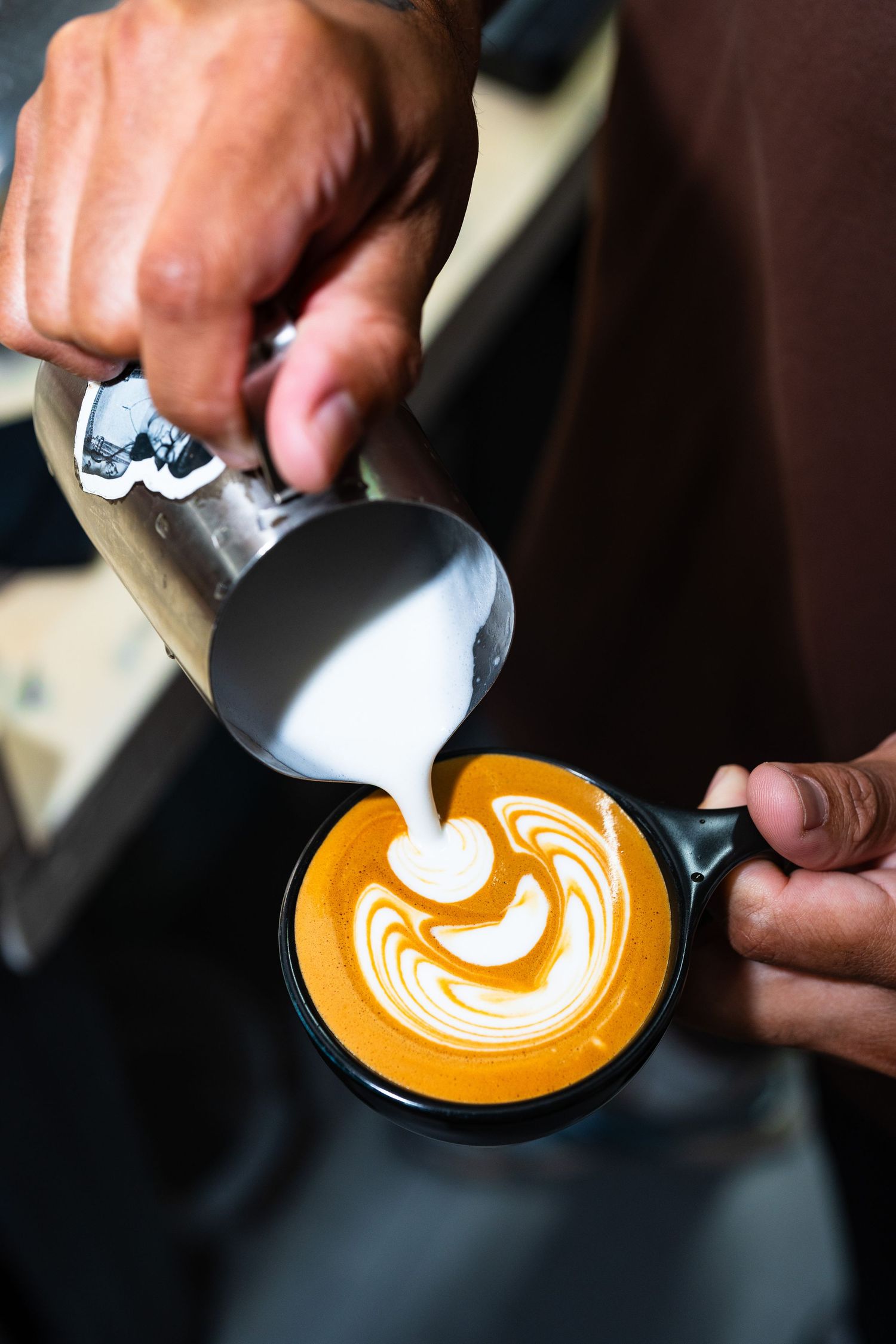 Barista pouring steamed milk into a latte cup, creating intricate latte art with a swirl pattern.