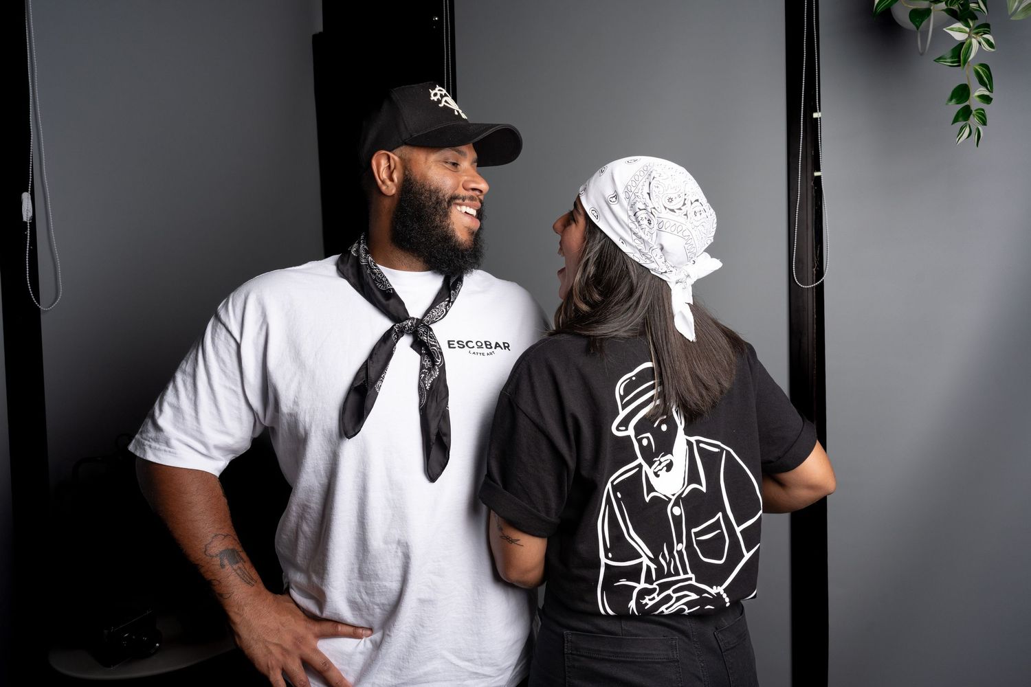 Two bartenders in matching Escobar black and white uniforms smiling at each other in a stylish bar setting.