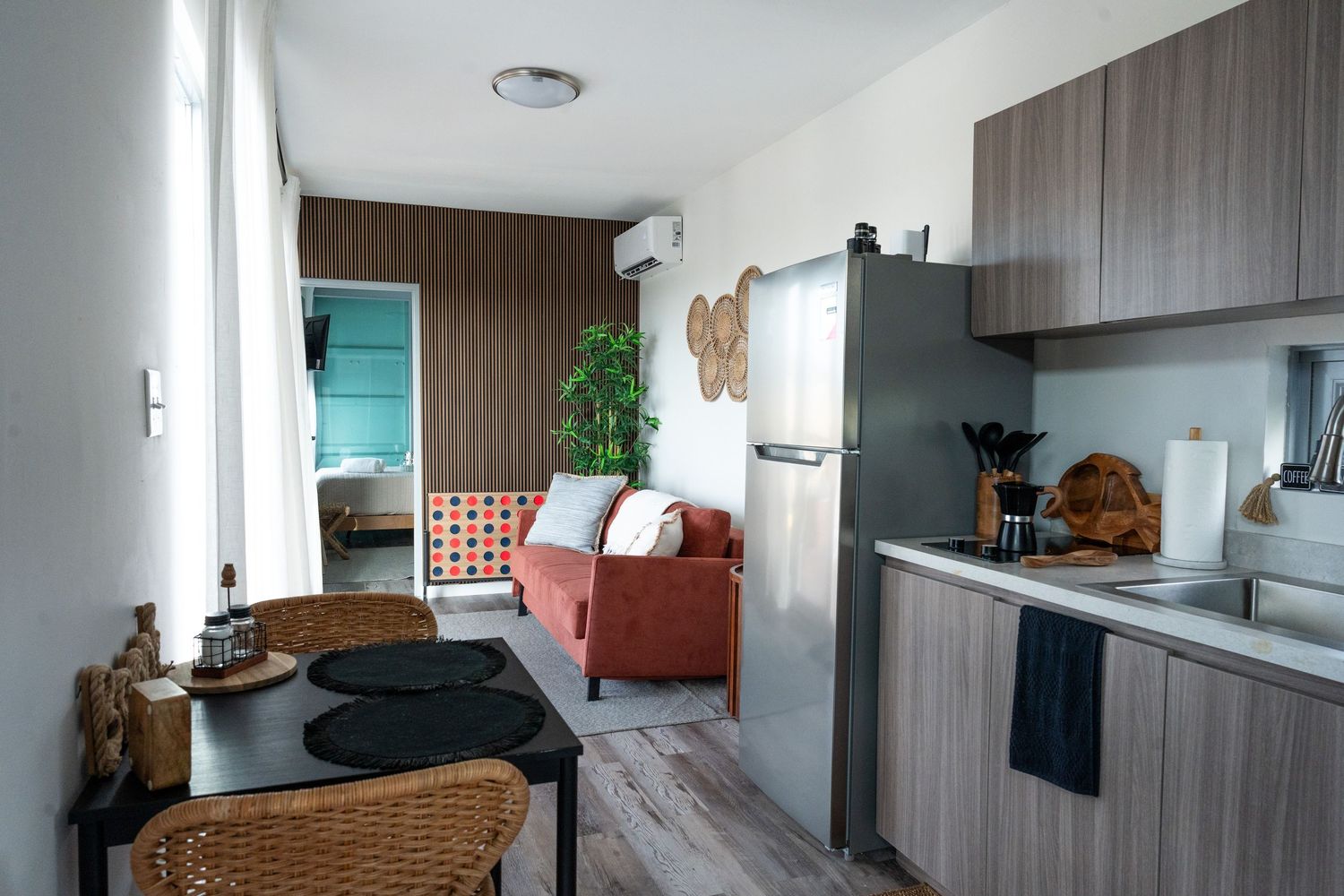 Compact studio apartment with open kitchen, red sofa, and wood-paneled accent wall.