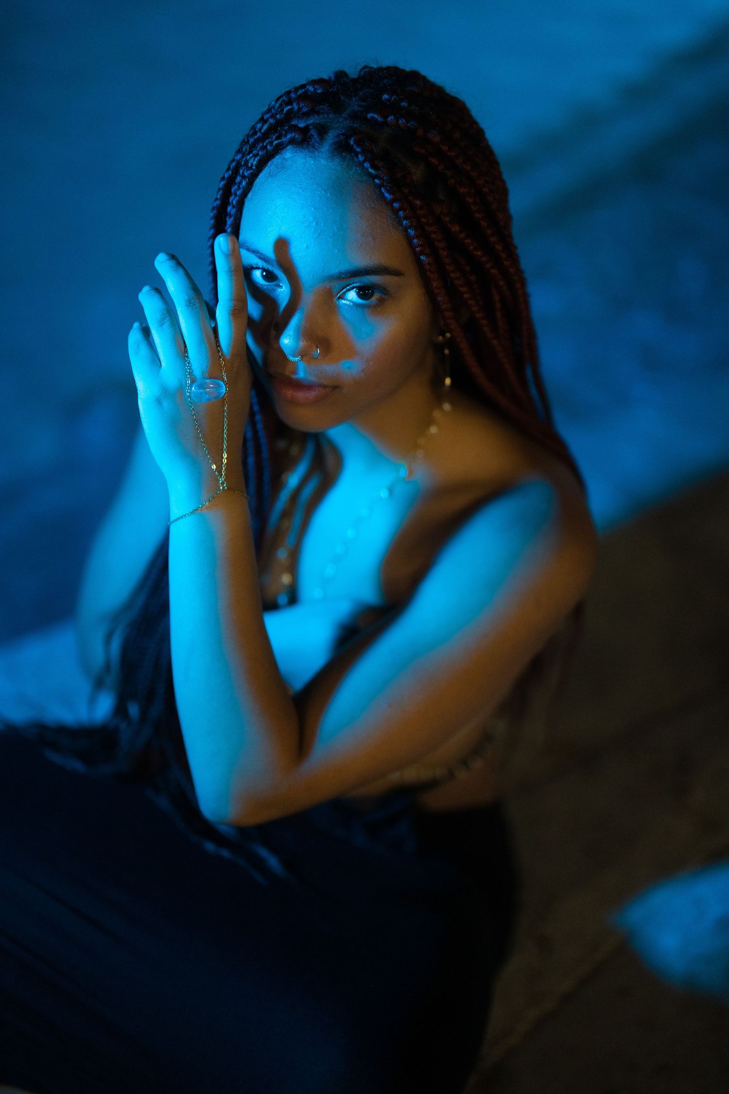 Mysterious woman with braided hair holding necklace under dramatic blue light in dark setting.