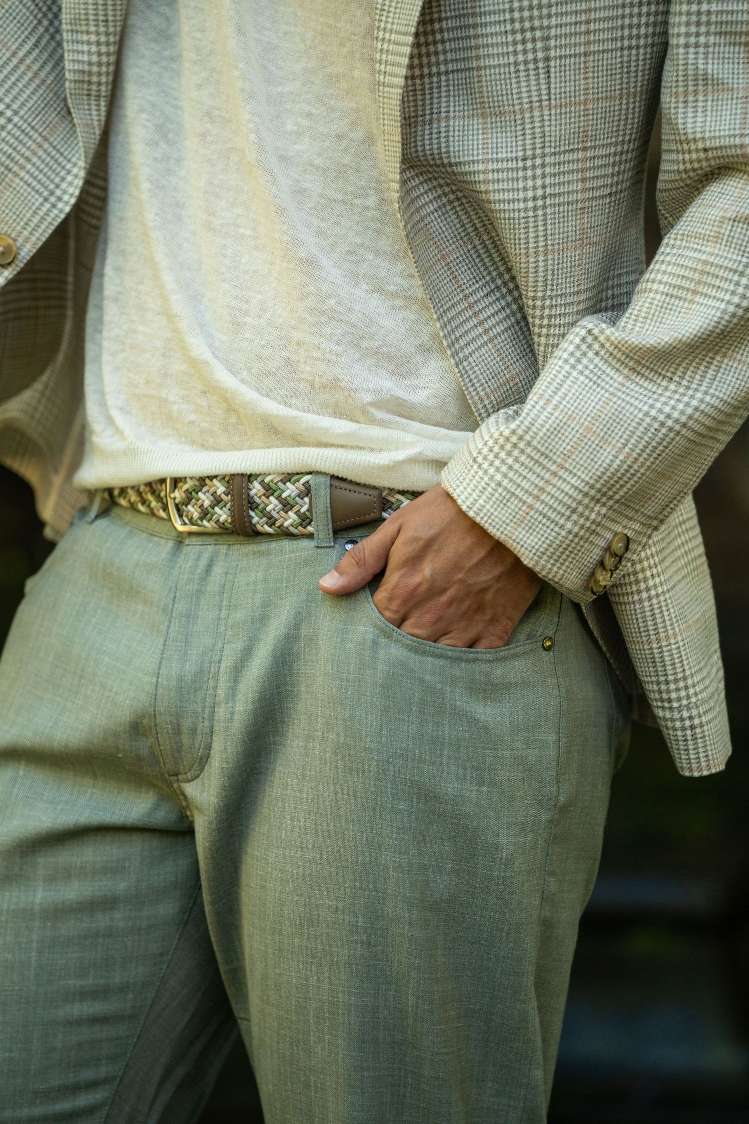 Close-up of mens sage green trousers with woven belt and plaid blazer.