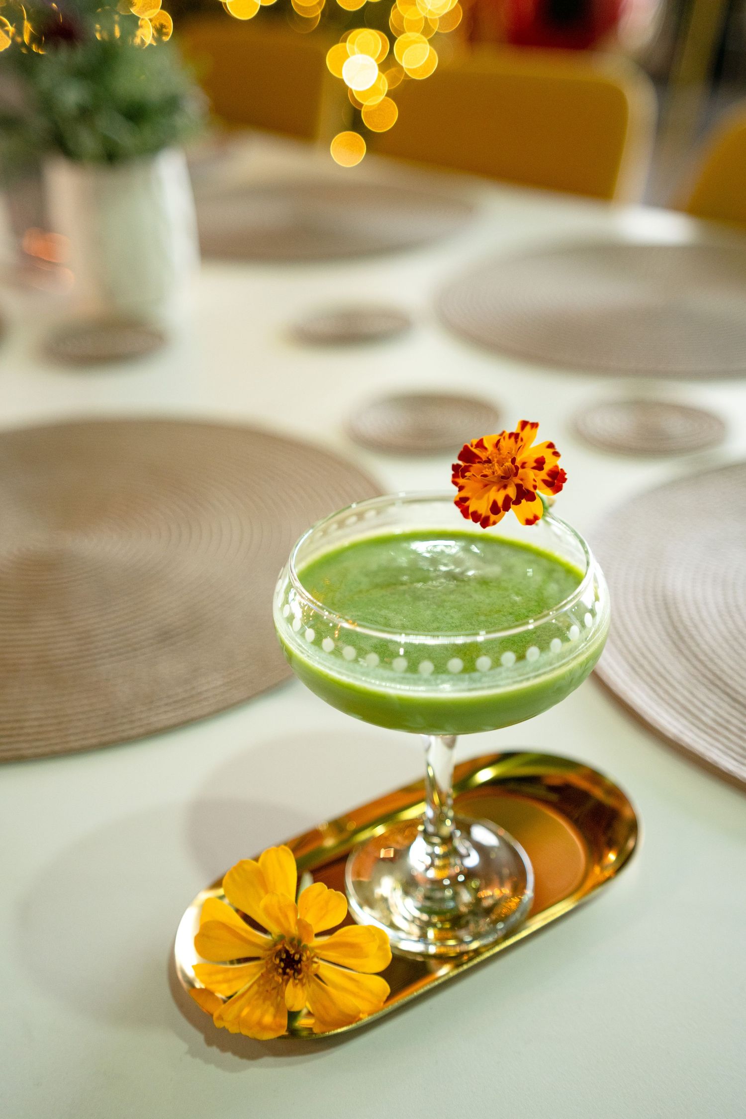 Green matcha cocktail in coupe glass garnished with marigold flower on gold tray.
