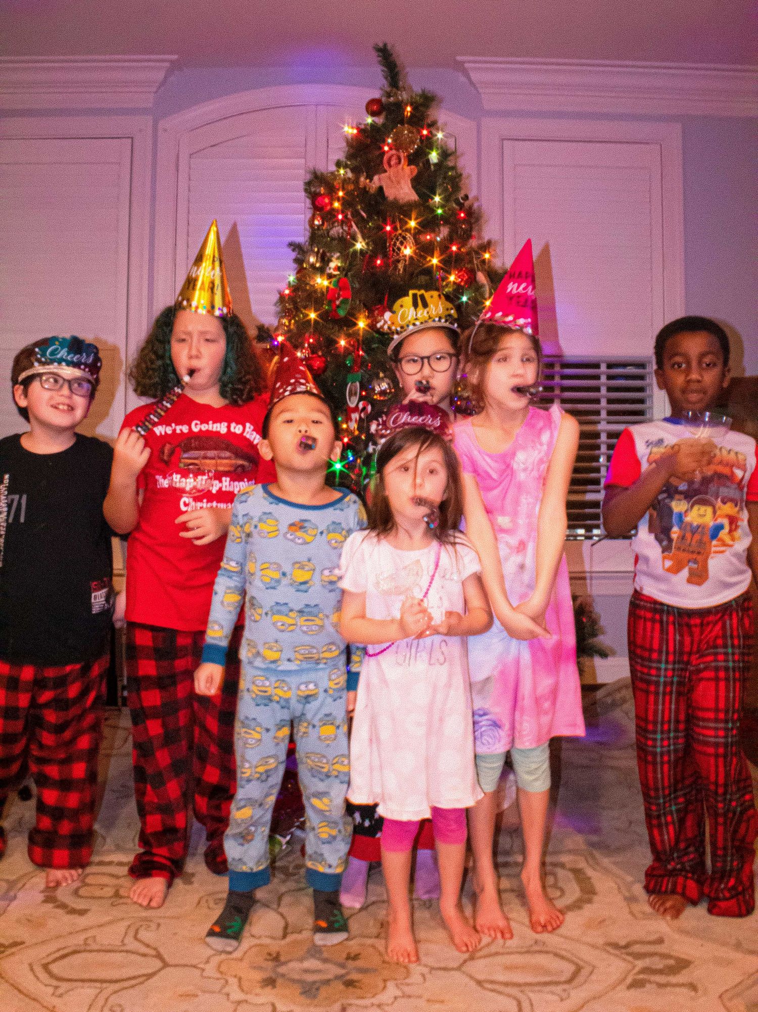 Kids in pajamas and party hats lined up for a holiday photo with Christmas tree.