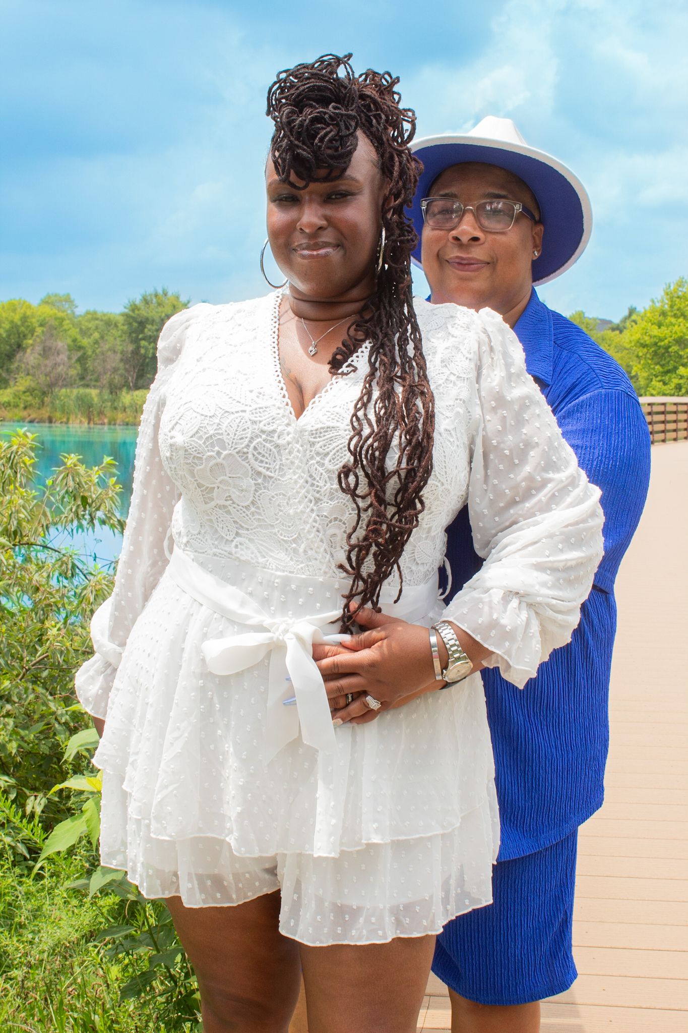 Couple in coordinated white and blue outfits posing together on boardwalk with water views.