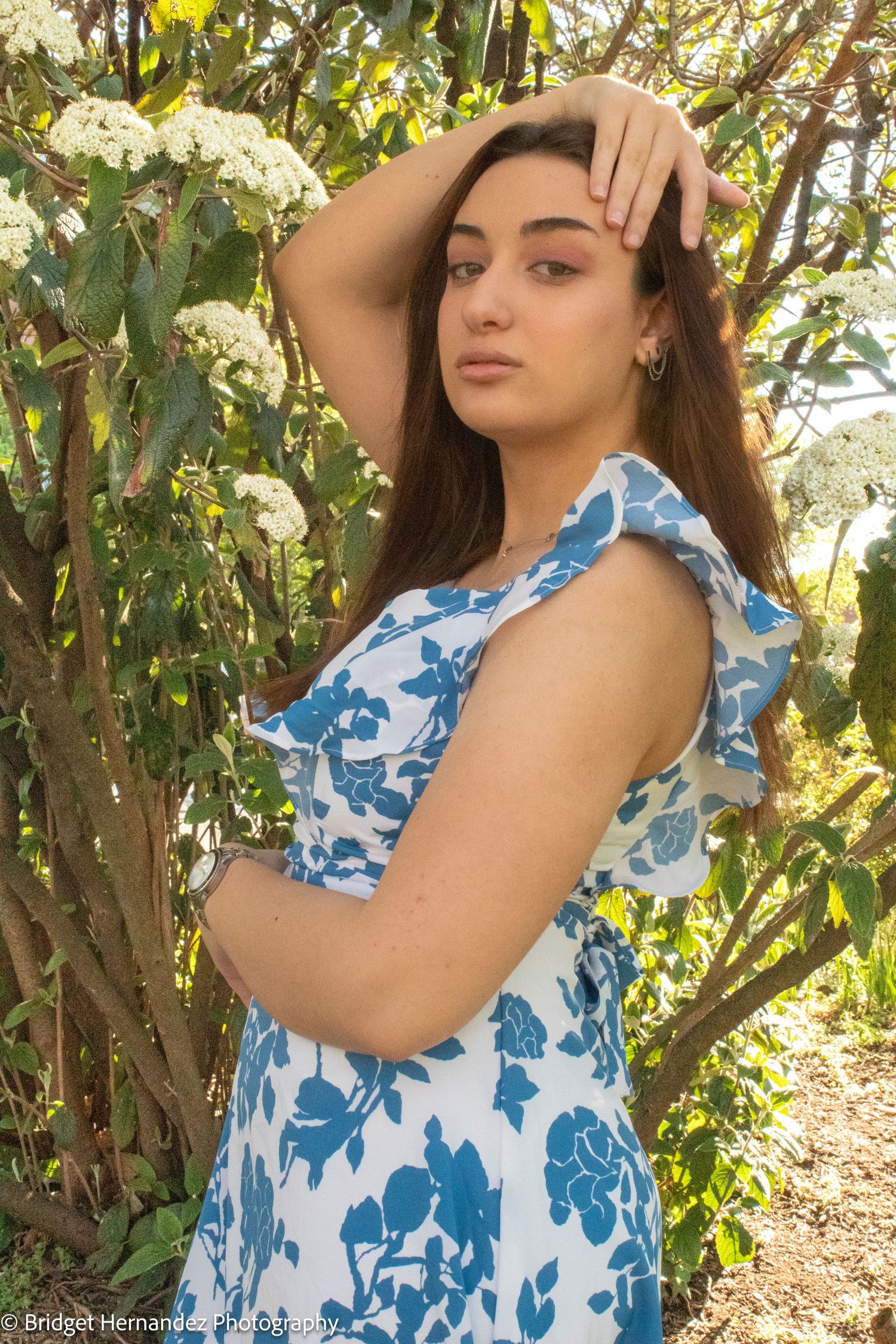 Fashion portrait in blue floral dress against white flowering bushes.