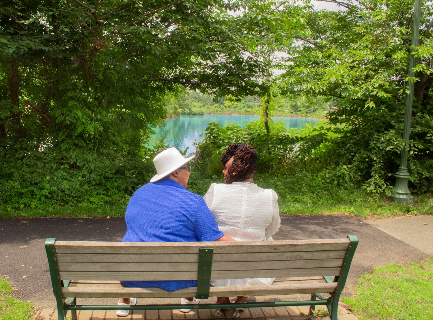 People sitting together on green park benches surrounded by lush trees and grass.