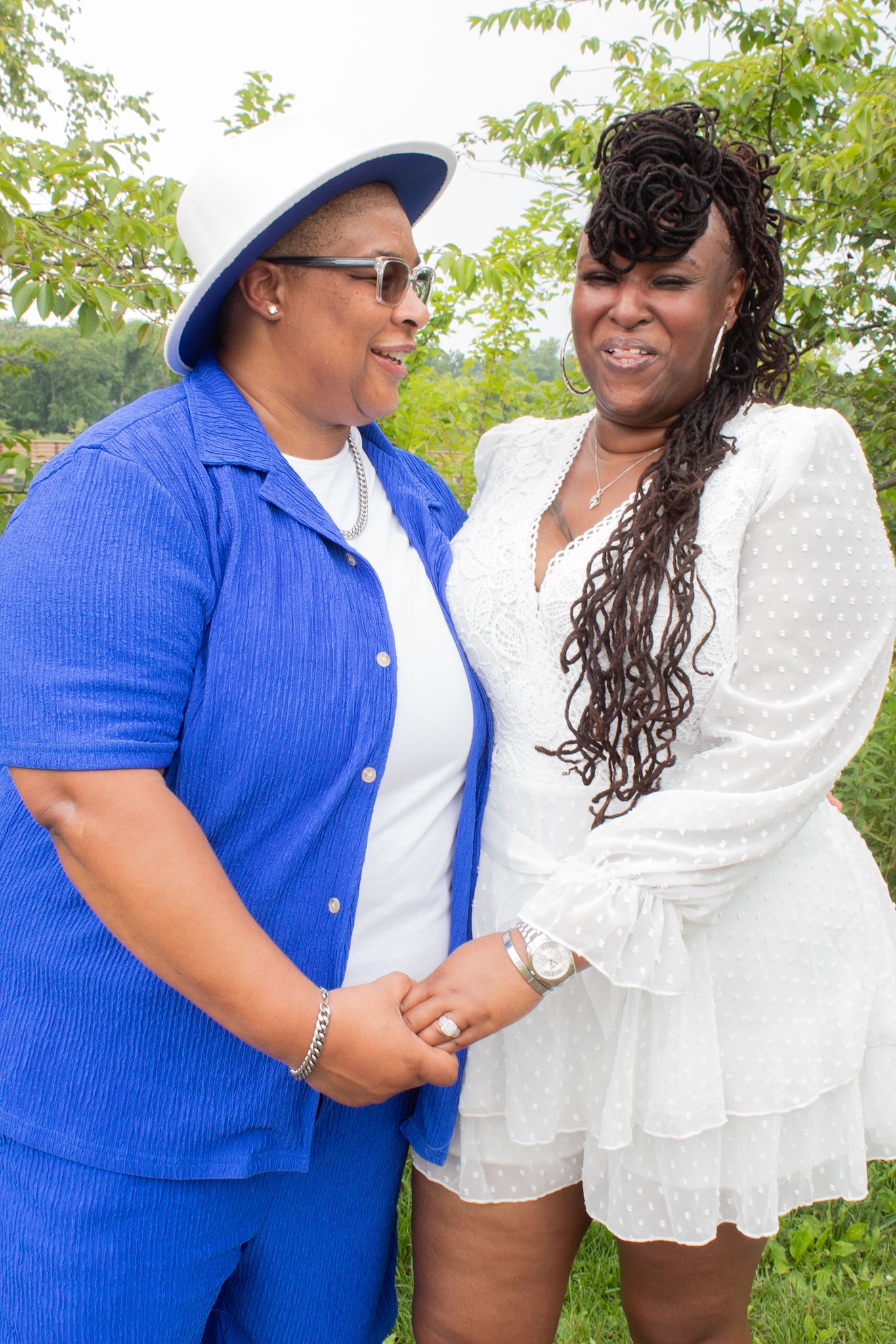 A couple wearing matching blue and white outfits smiling and holding hands in a natural outdoor setting.