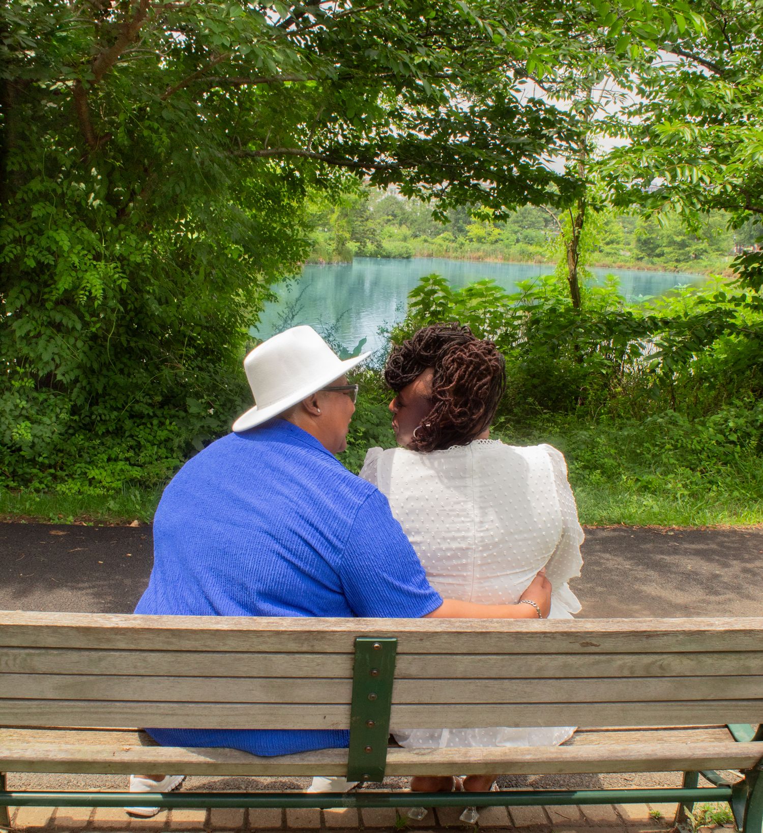 Couple sitting together on a park bench surrounded by lush green trees.