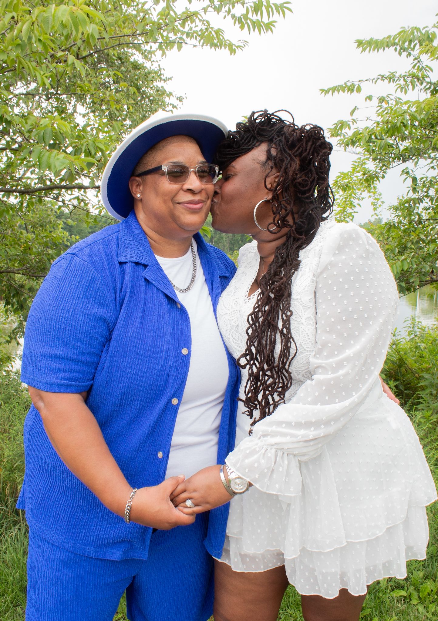 A couple in coordinated outfits showing affection while standing on a path surrounded by trees.