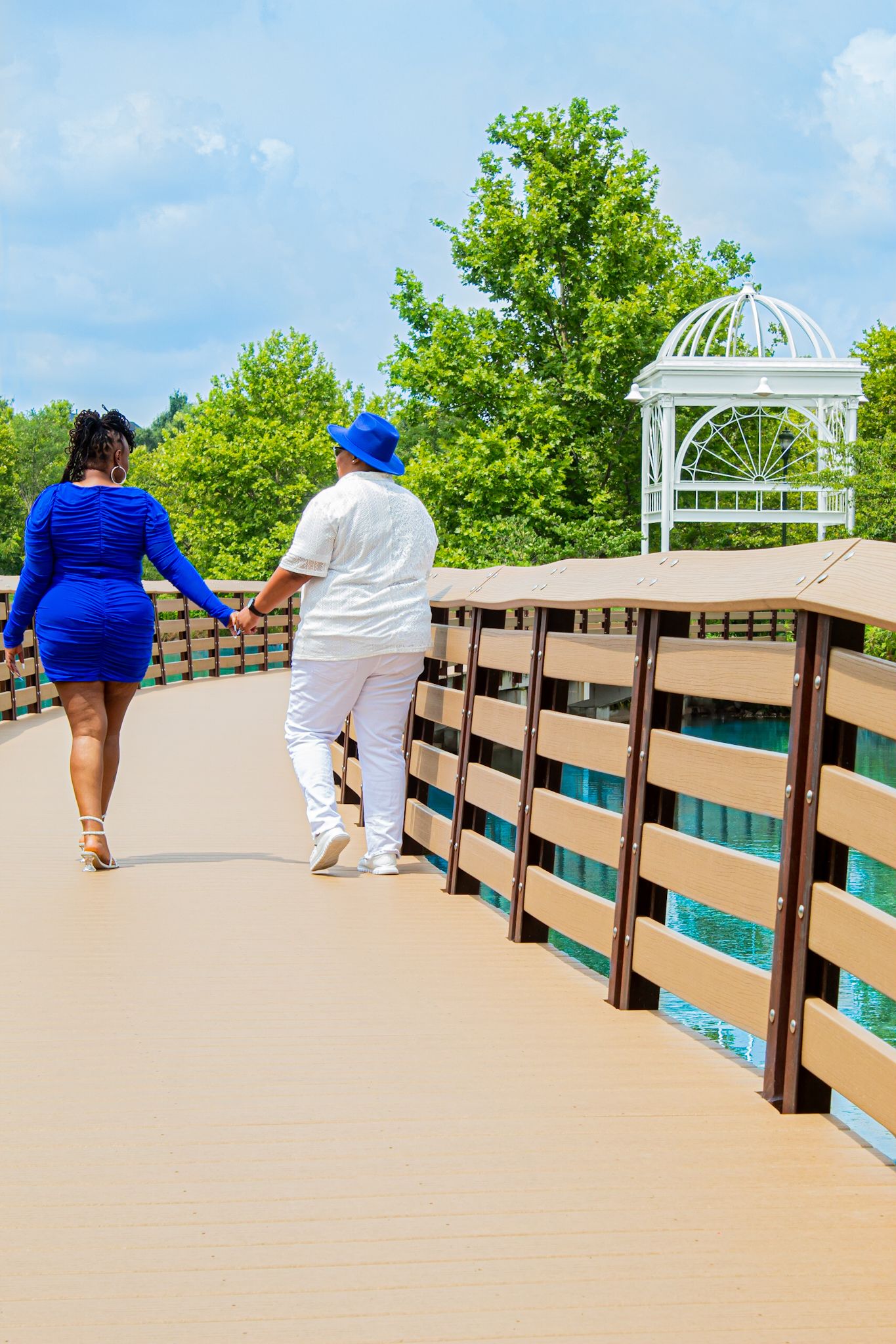 Couple walking along wooden boardwalk towards white gazebo on sunny day.