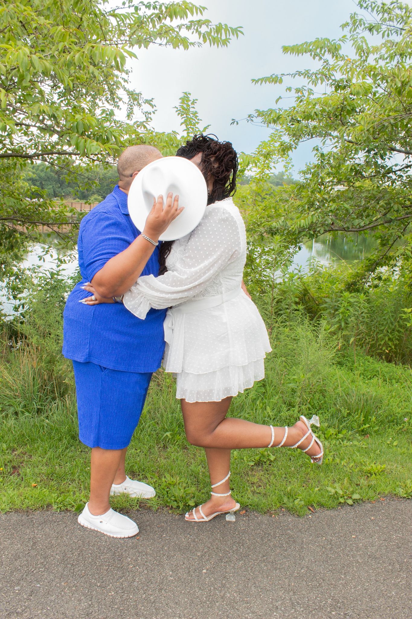 Two people in coordinating blue and white outfits embracing on a path with lush greenery in background.